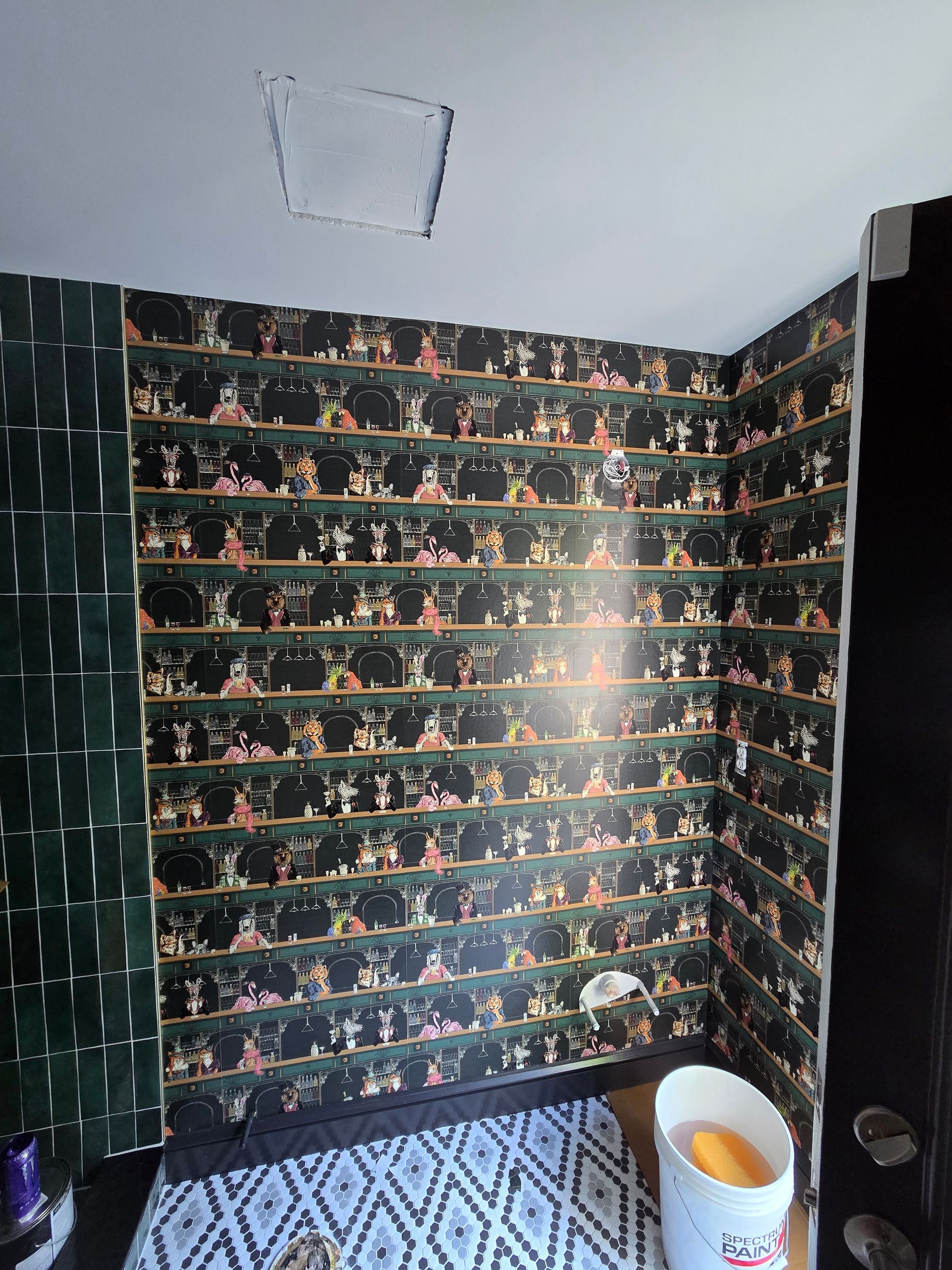 A corner of a room featuring dark, patterned wallpaper with multiple horizontal rows of small, colorful figures.