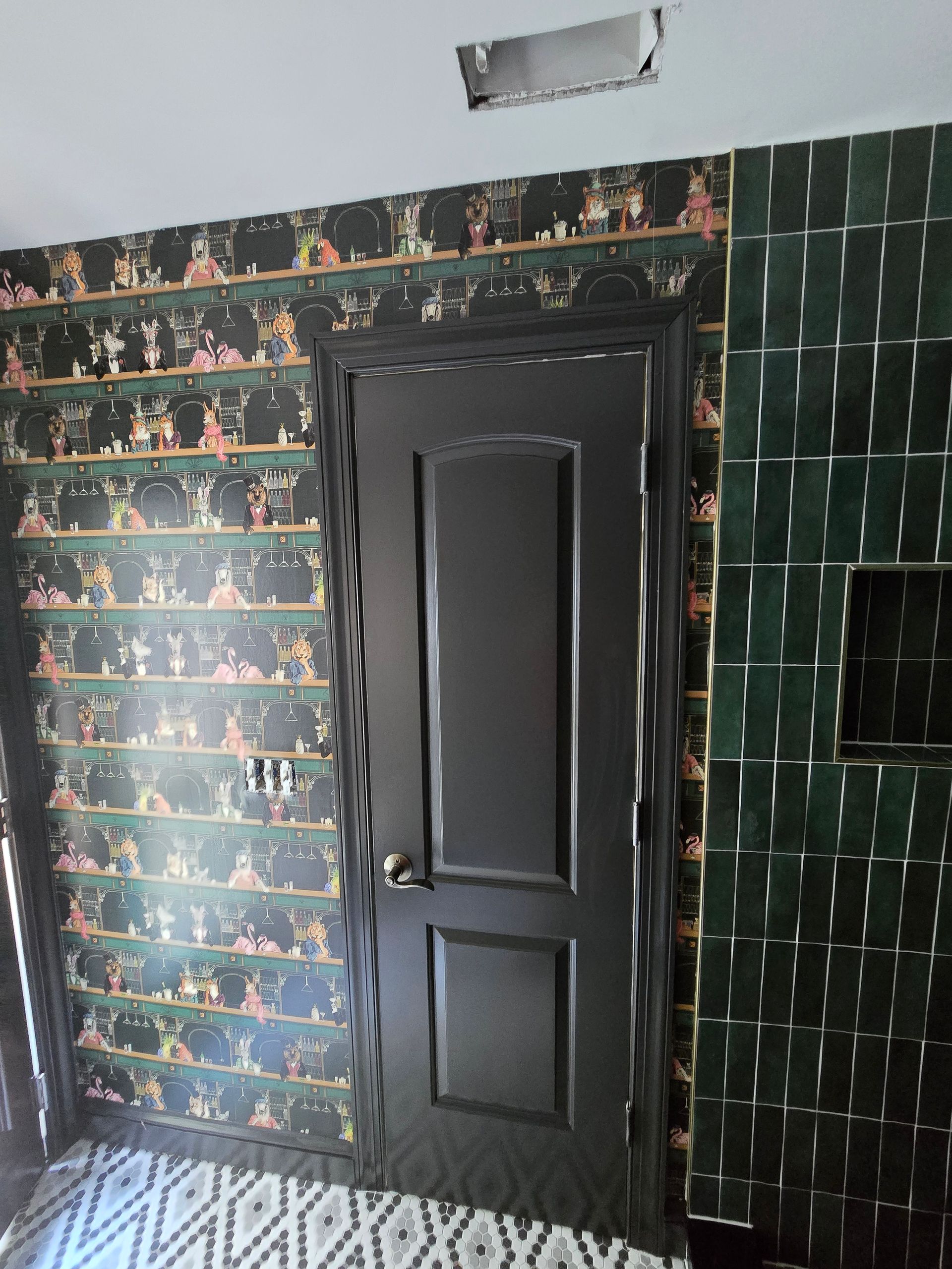 A black door sits between a patterned, green-themed wallpaper and a dark green, rectangular tiled wall.