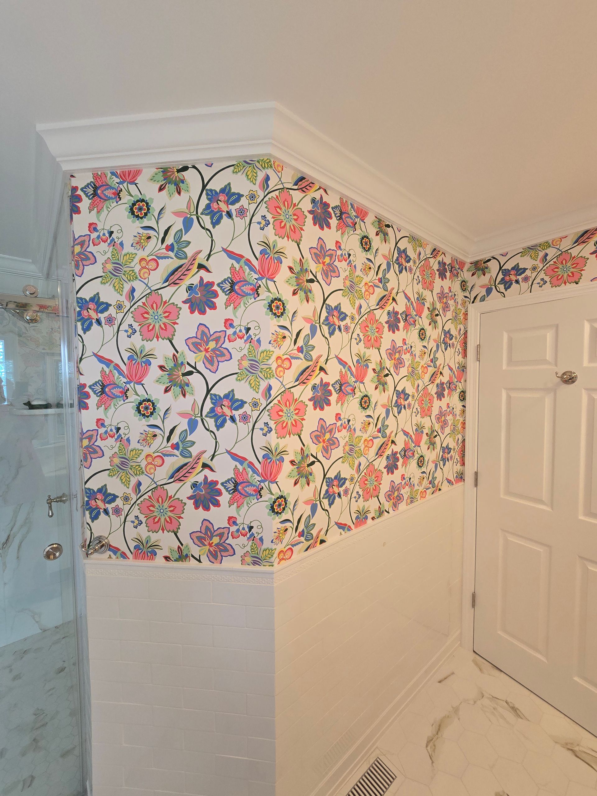 A room corner featuring white wainscoting topped with vibrant floral wallpaper and crown molding near a white door.