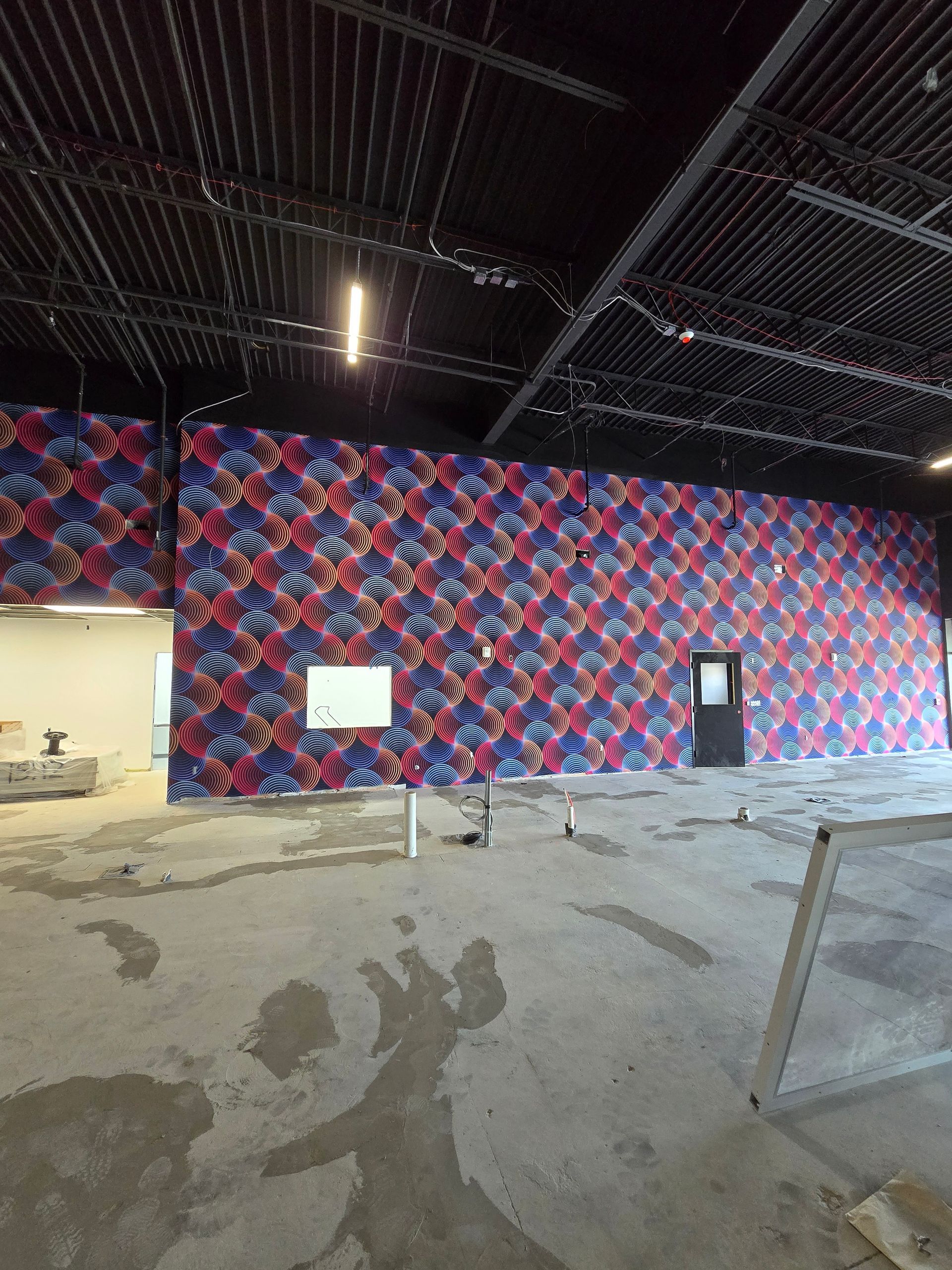 A wide wall in an unfinished industrial space covered in a colorful, repeating plaid pattern in blue, red, and white.