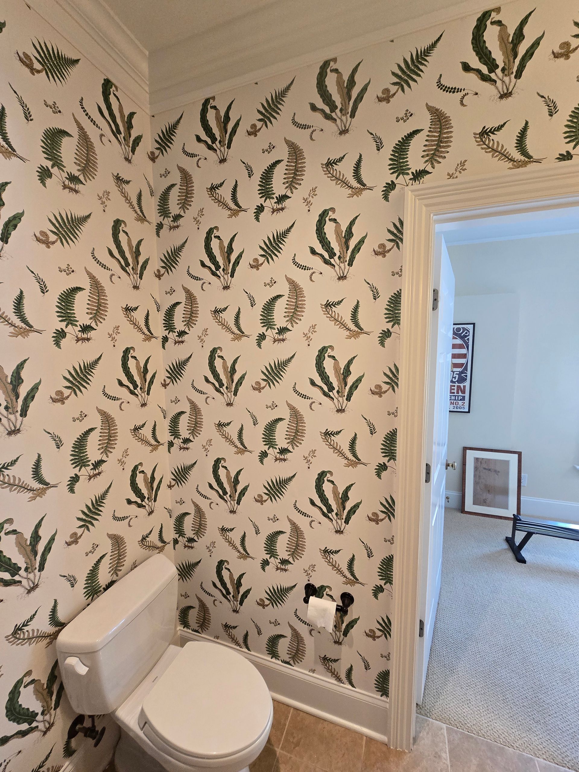 A white toilet sits in a small room with cream wallpaper featuring a repeating green and brown fern leaf pattern.