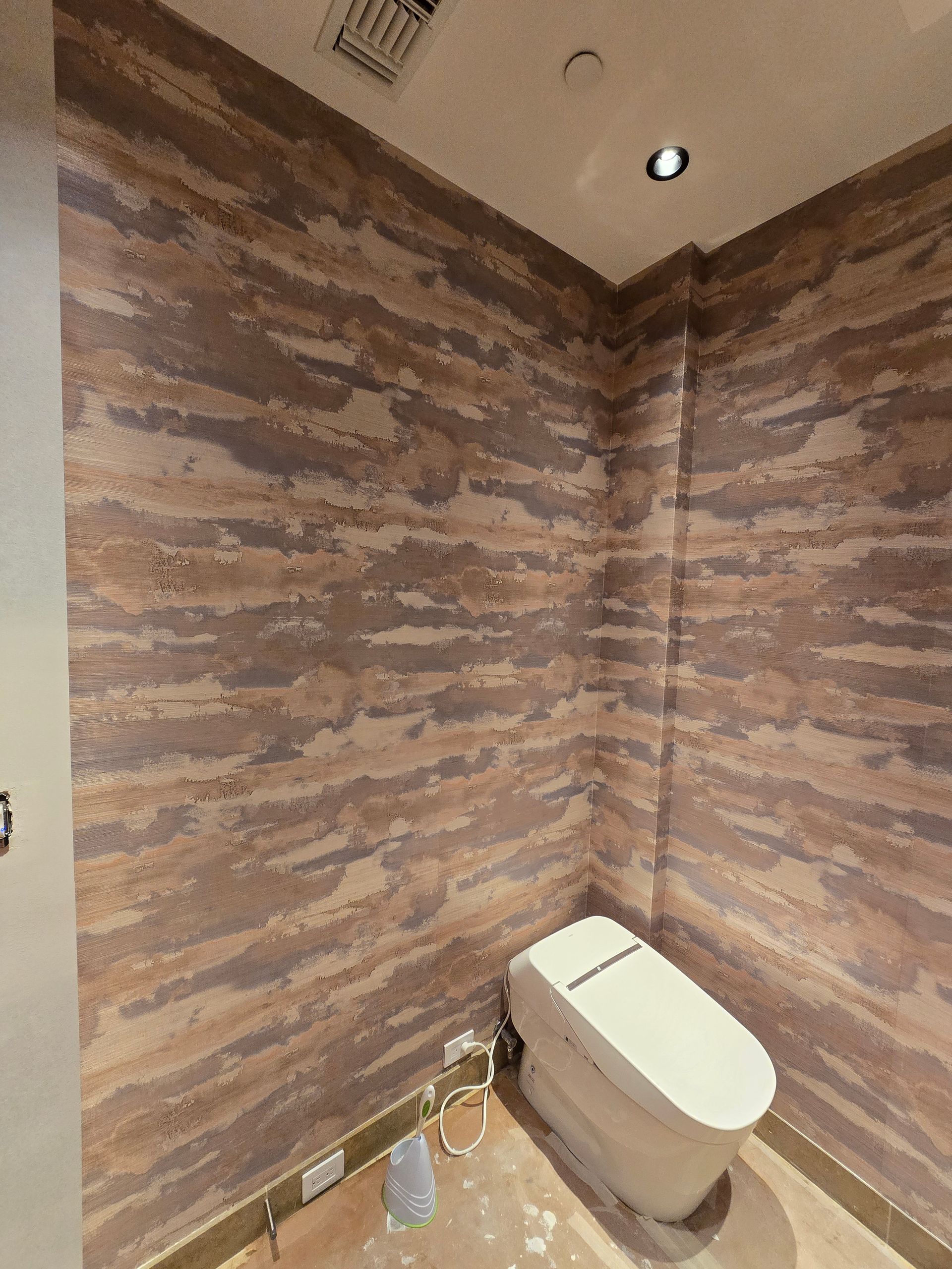 A modern white toilet in a corner with textured, horizontal-striped wallpaper in shades of brown, tan, and gray.