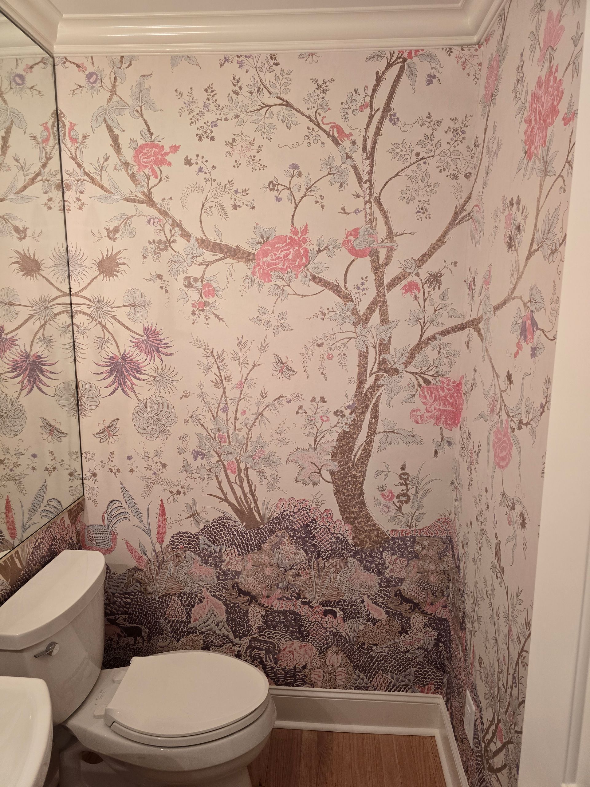 A small bathroom wall covered in light wallpaper featuring a large, ornate tree with pink flowers and a dark landscape base.