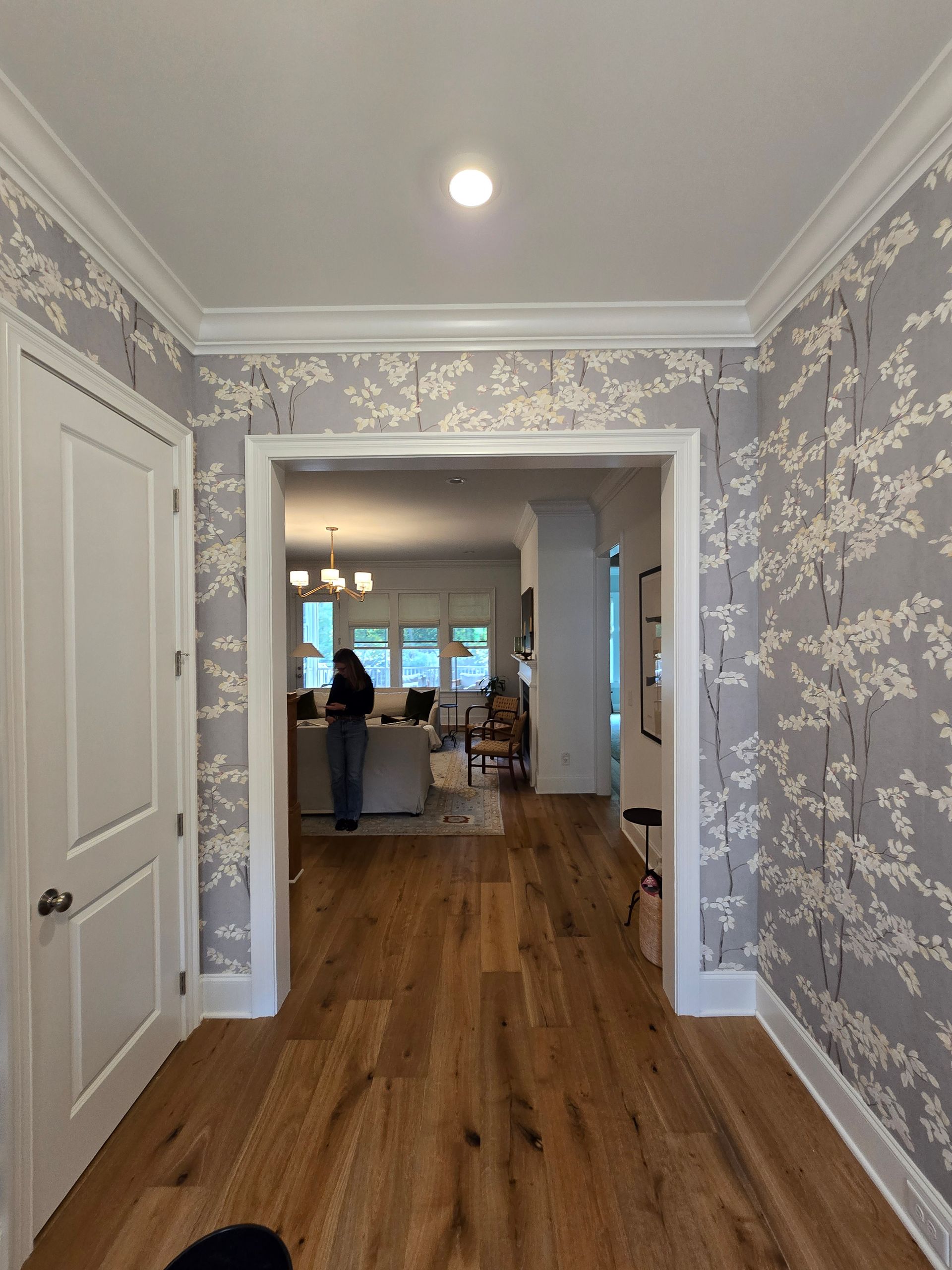 A hallway with gray floral wallpaper and wood floors leading into a living area.