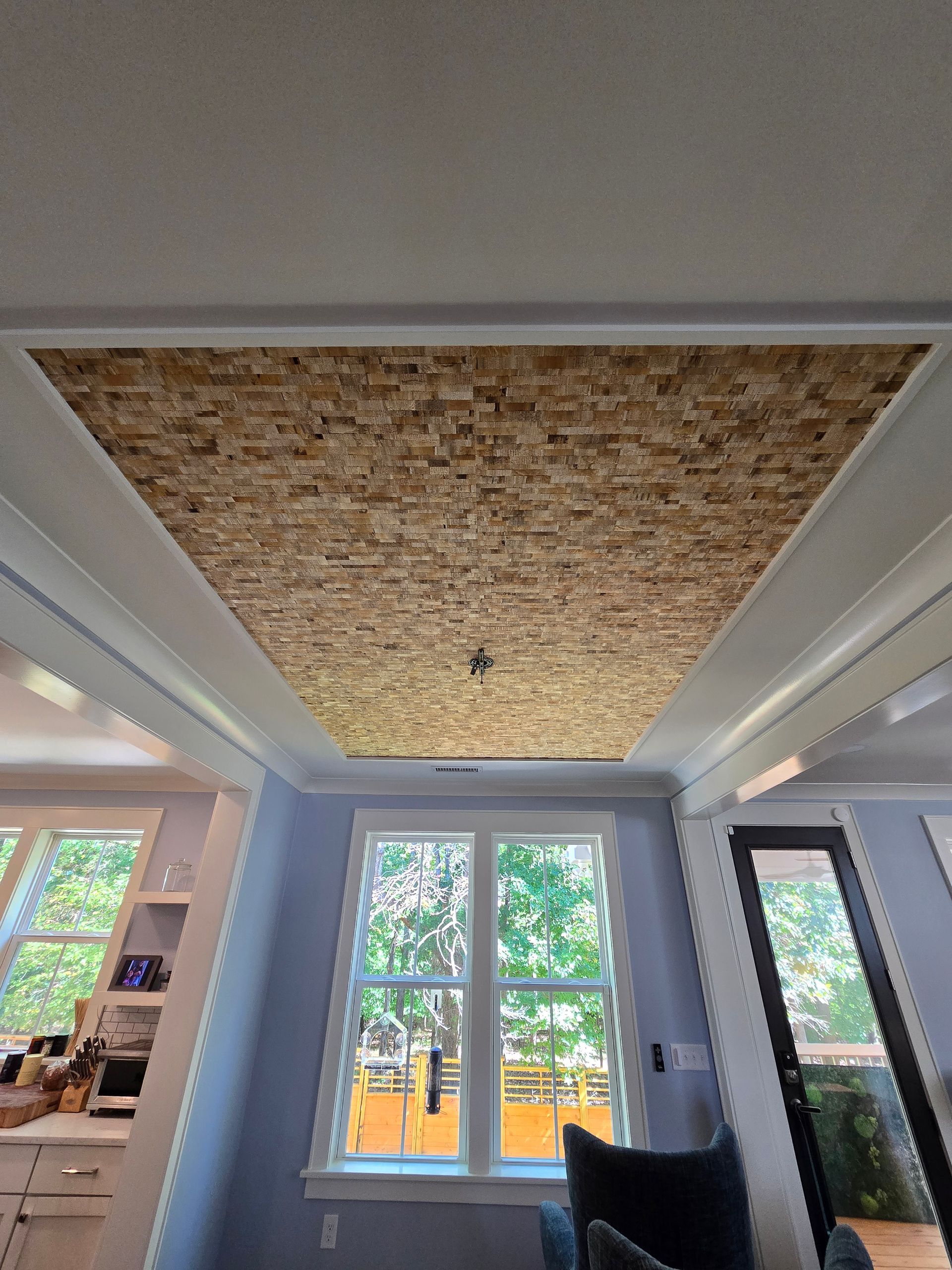 A partially finished ceiling tray featuring an exposed oriented strand board (OSB) panel framed by white trim in a room.