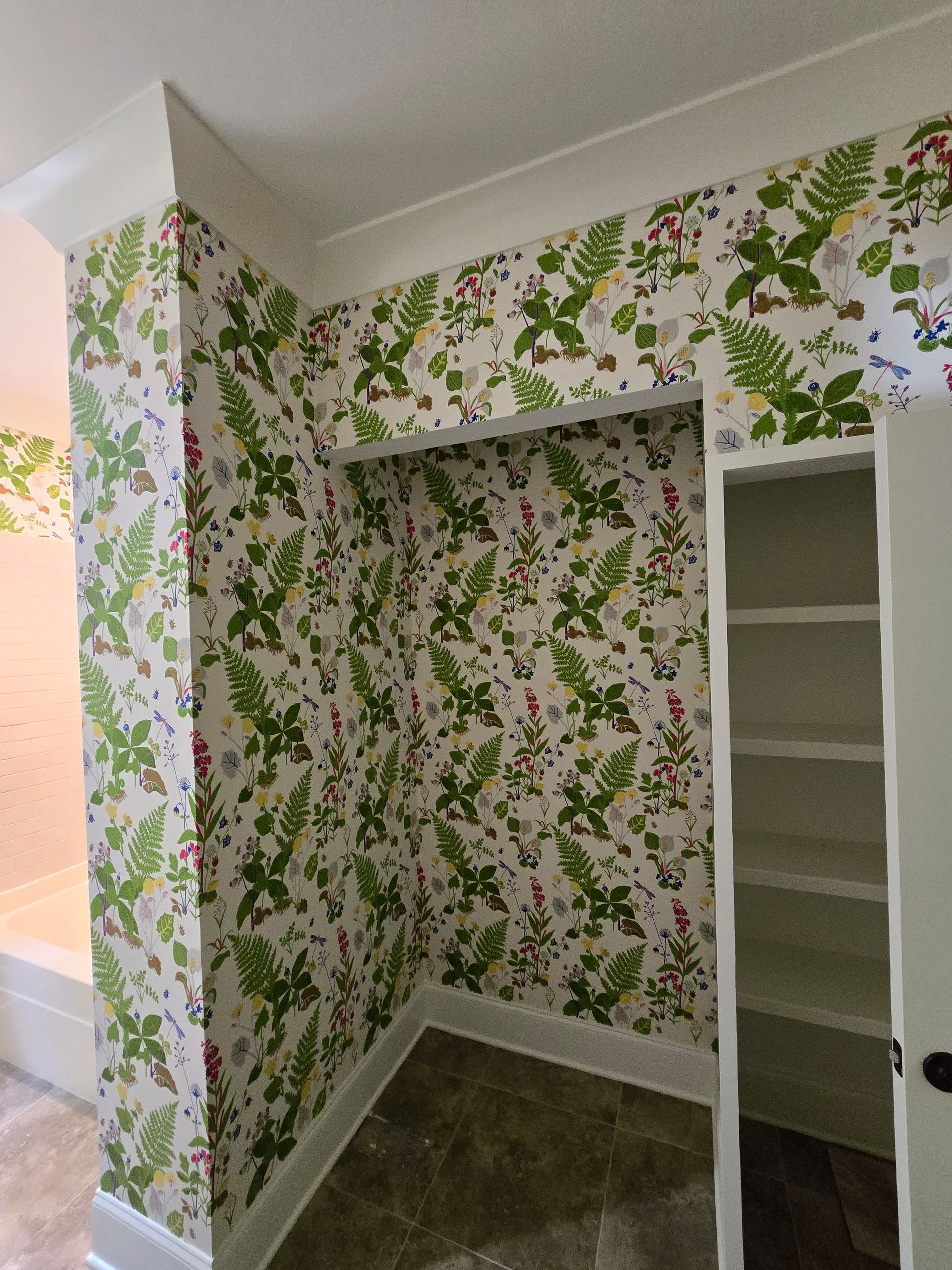 An alcove and adjacent wall are covered in botanical-print wallpaper featuring green ferns, leaves, and small red berries.