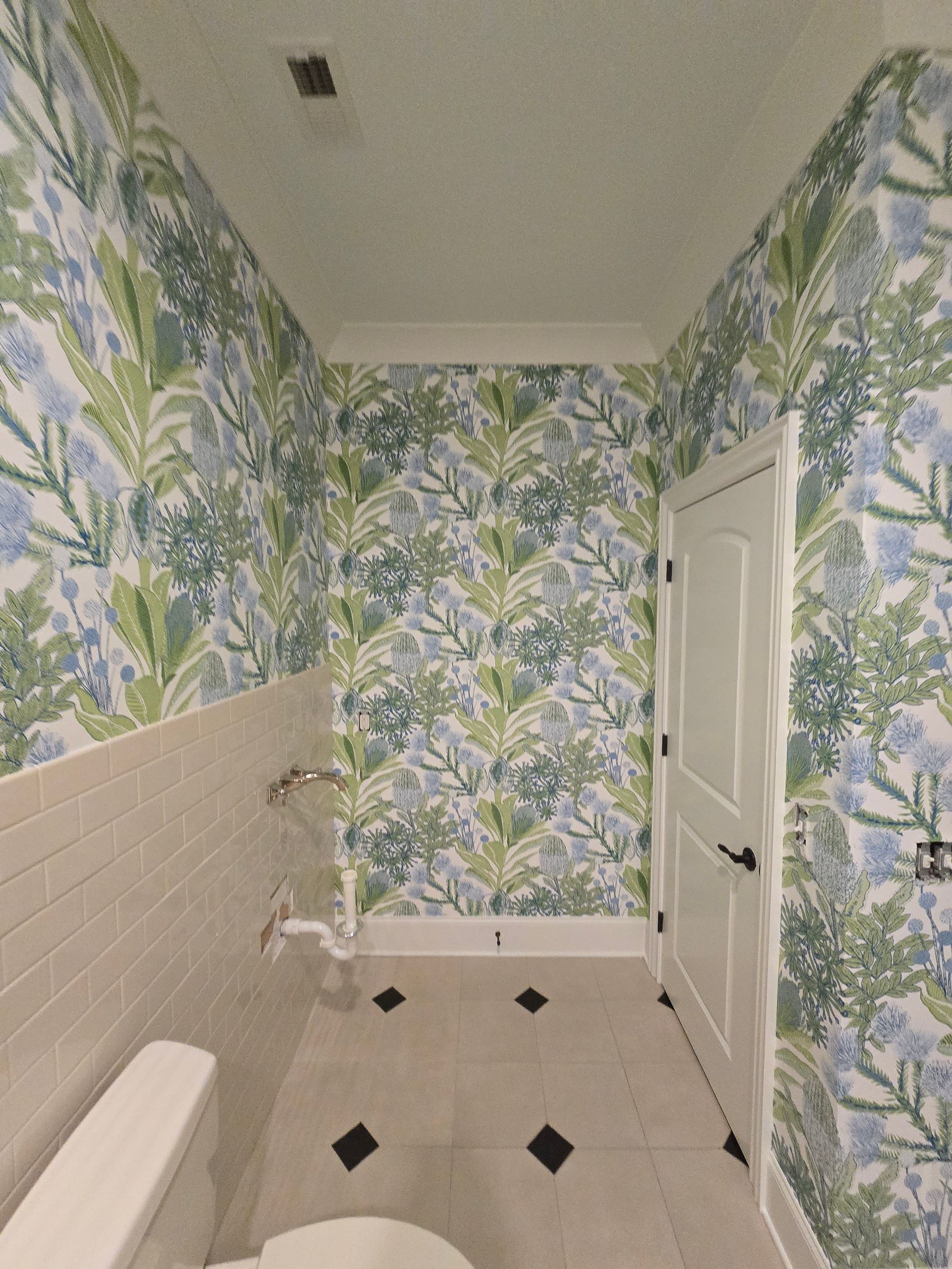A small bathroom with floral wallpaper, white subway tile wainscoting, and white floor tiles with black diamond accents.