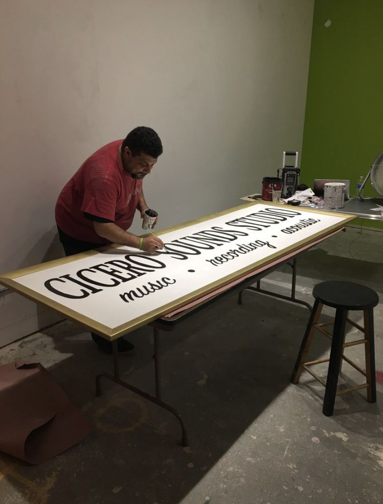 A man in a red shirt is painting a sign that says cicero music