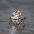 A gold ring featuring a central diamond surrounded by a filigree floral pattern accented with small, multicolored gems.