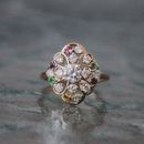A gold ring featuring a central diamond surrounded by a filigree floral pattern accented with small, multicolored gems.