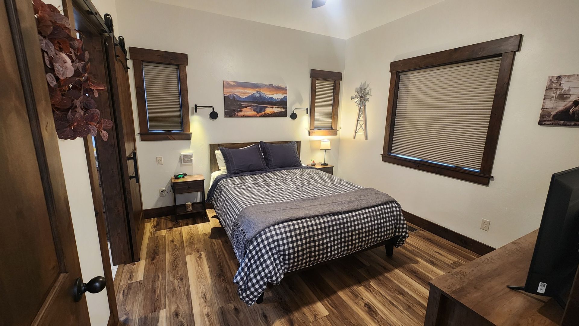 Bedroom with bed, two side tables, wooden floors, and framed windows.