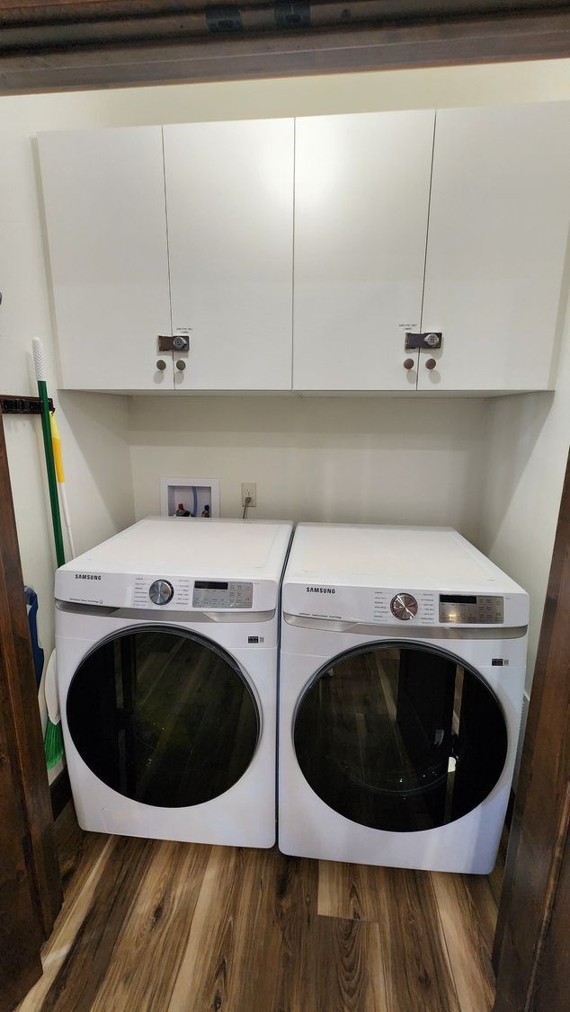 A white washer and dryer with overhead cabinets in a laundry room with wood-look flooring.