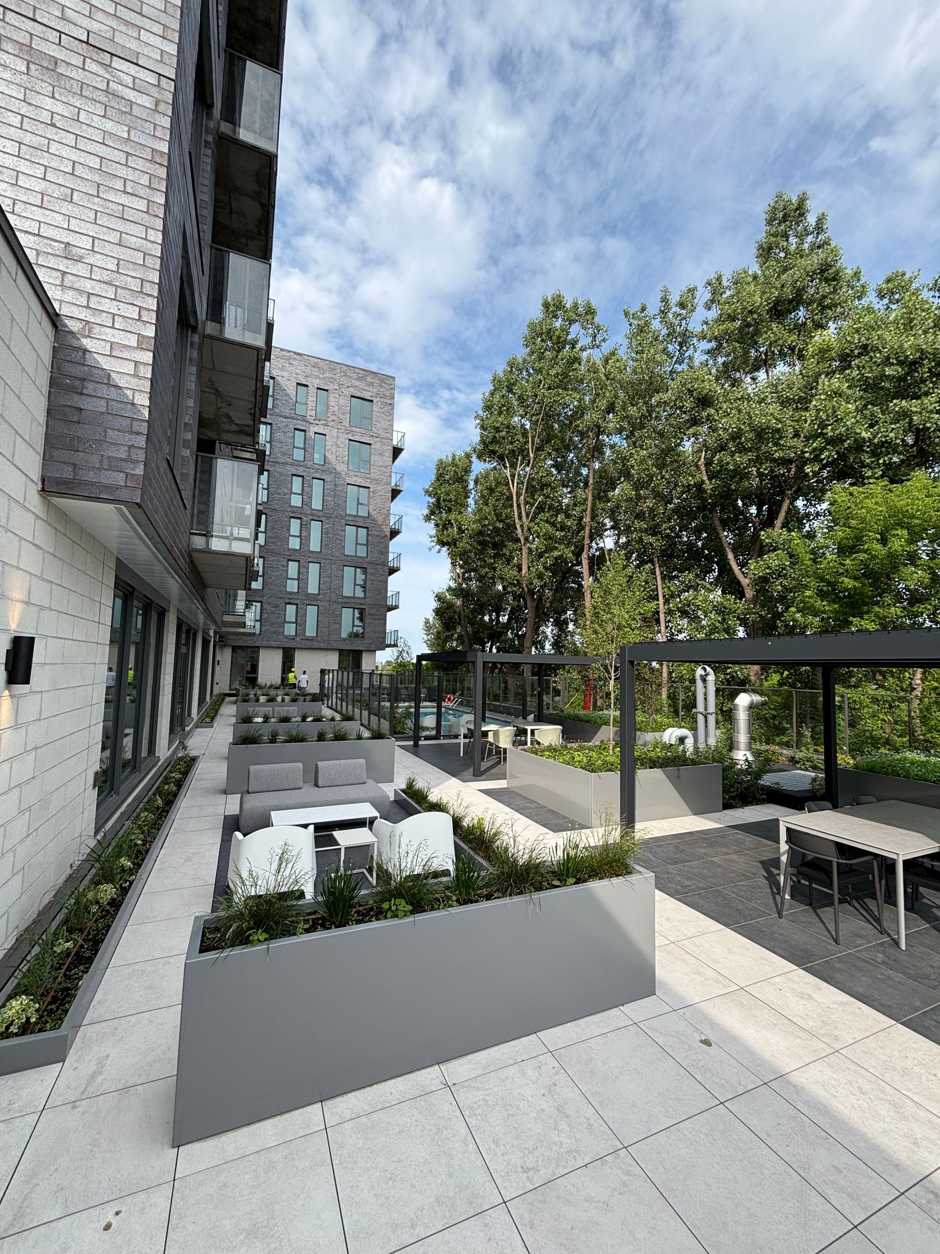 Terrasse extérieure avec sièges, à proximité de bâtiments modernes et d'arbres, sous un ciel nuageux.