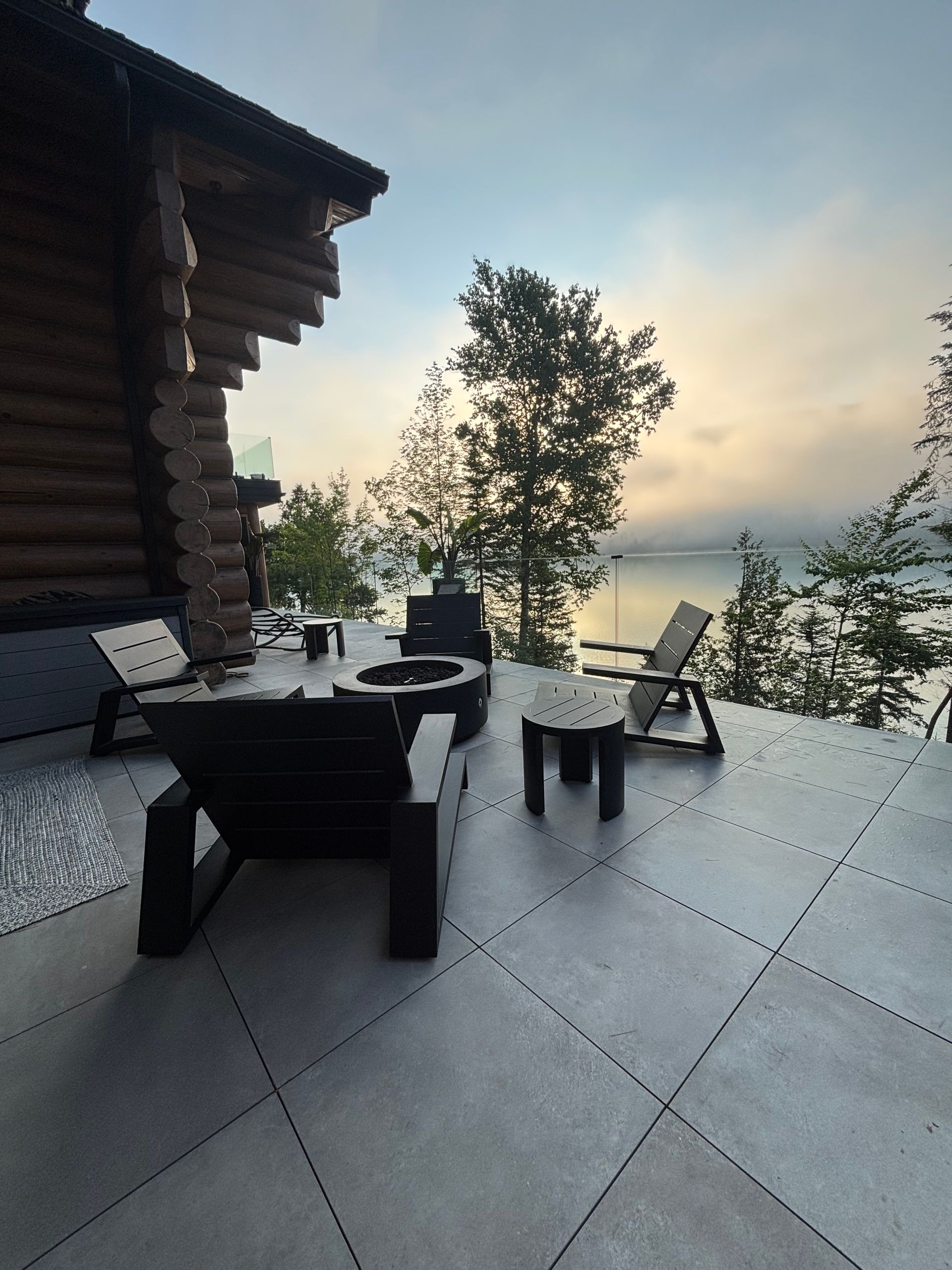 Terrasse avec mobilier sombre, donnant sur un lac calme au crépuscule, à côté d'un chalet en rondins.