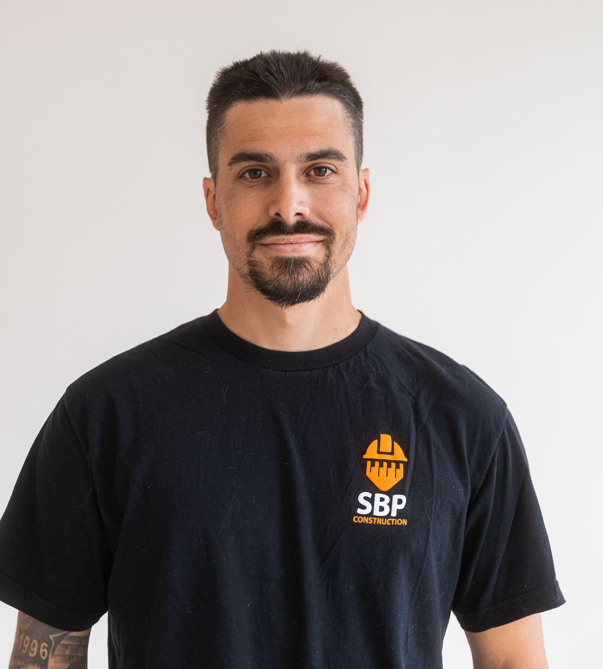 Man wearing a black t-shirt with a logo, smiling, and against a white background.