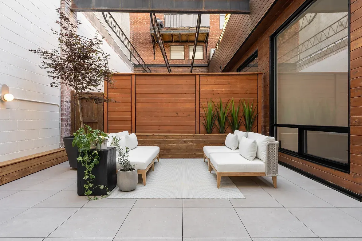 Un patio avec deux canapés blancs et une clôture en bois.