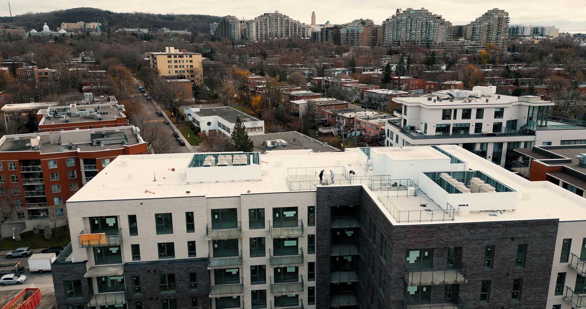 Aerial view of a partially constructed multi-story apartment building with a white flat roof and dark masonry siding.