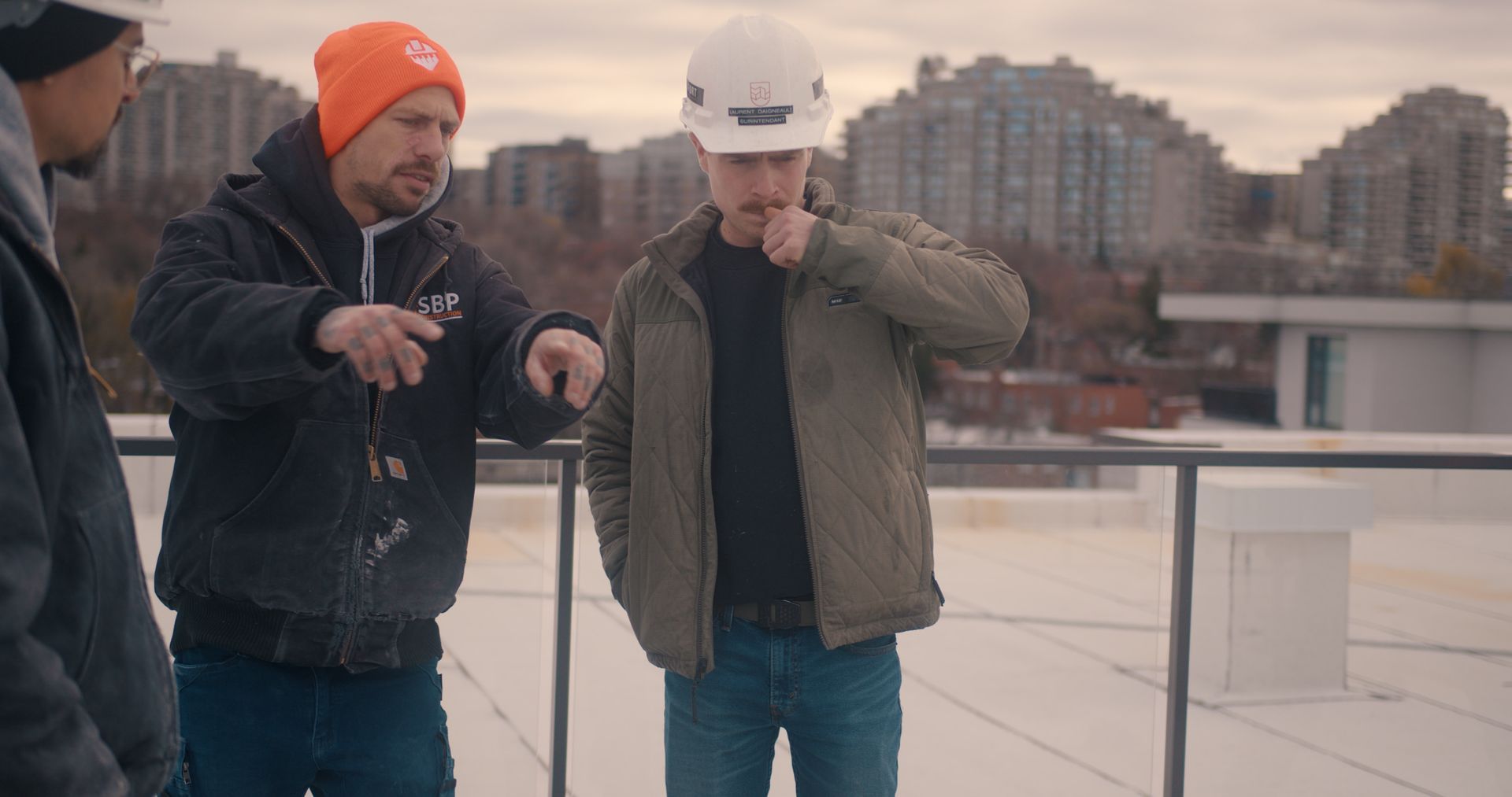 Trois personnes sur un toit, l'une d'elles portant un casque de chantier, pointant du doigt et discutant de quelque chose.