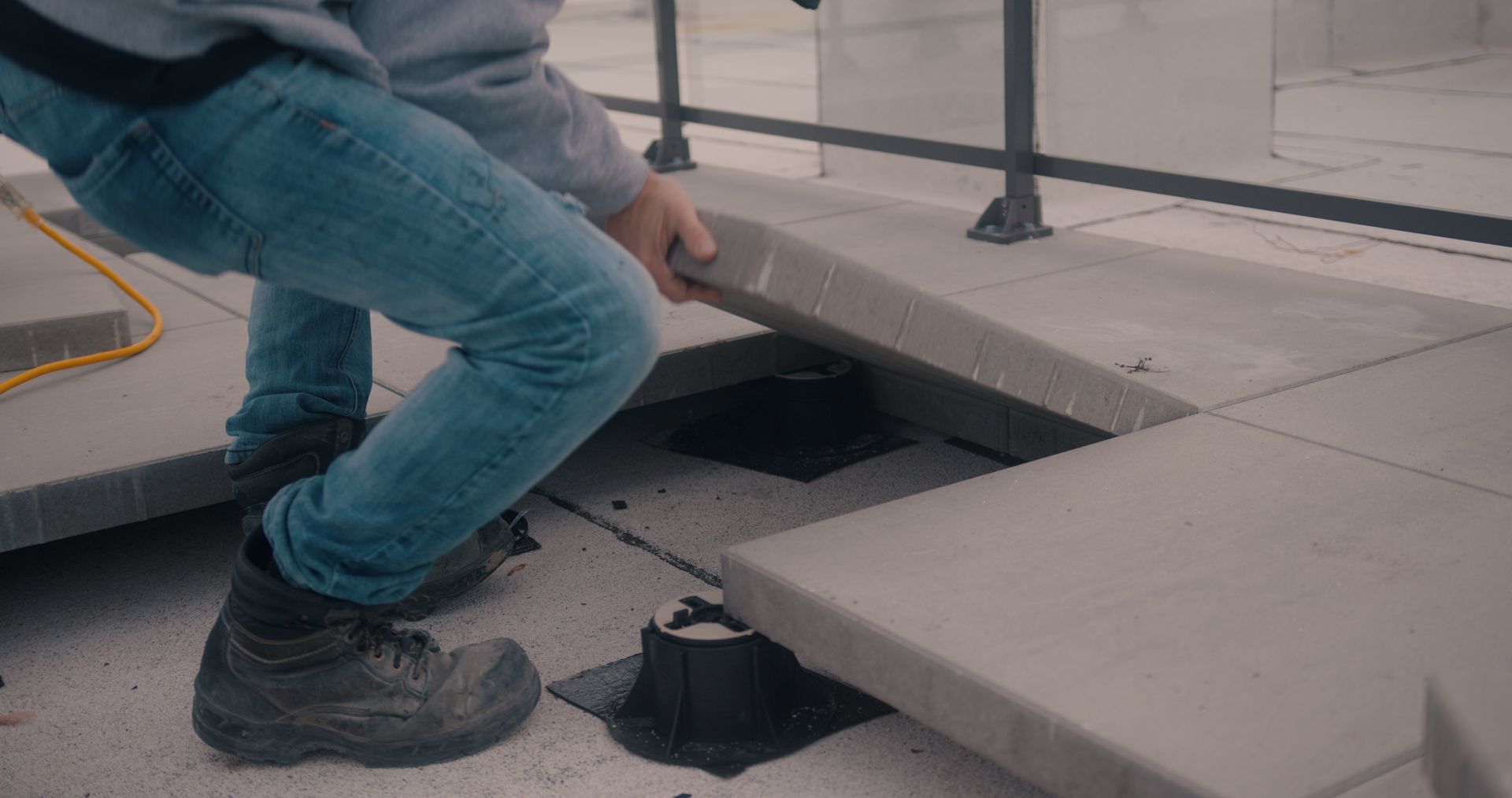 A worker installing or adjusting concrete pavers on an elevated rooftop pedestal system.