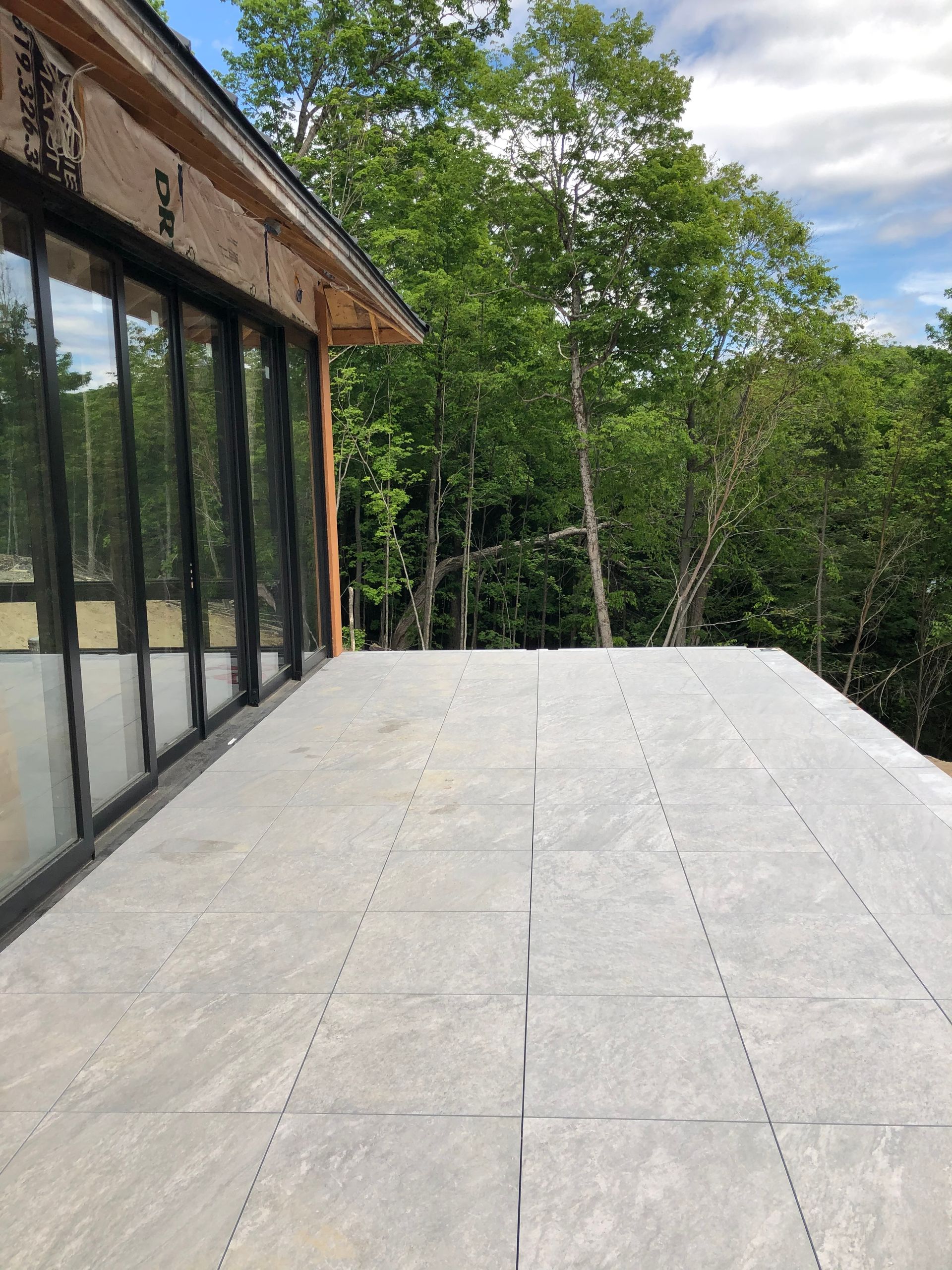 Vue d'une terrasse en pierre grise prolongeant une maison aux grandes portes vitrées, encadrée par une forêt verdoyante luxuriante.