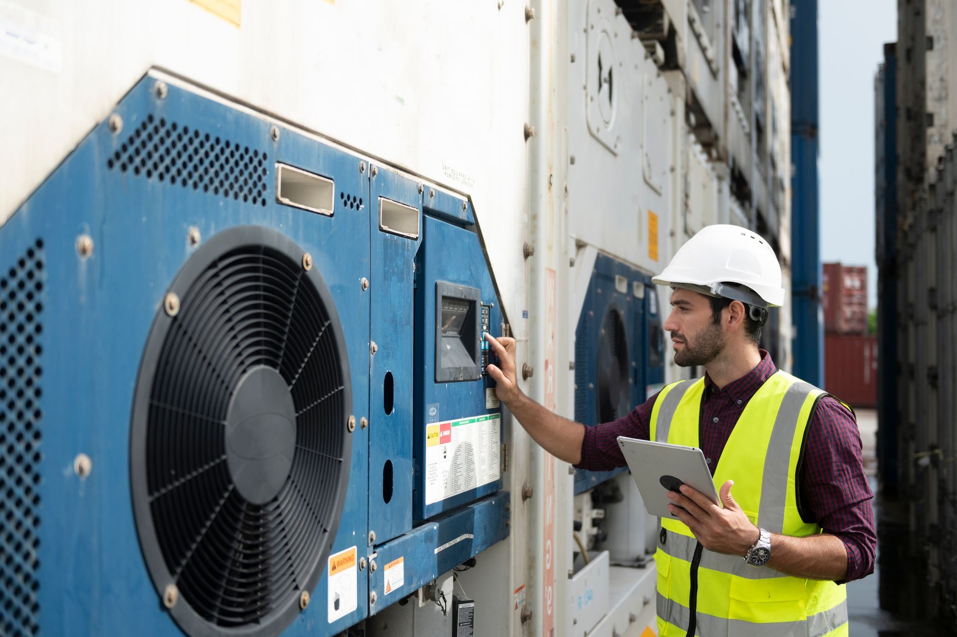 A man in a yellow vest and hard hat is looking at a machine.
