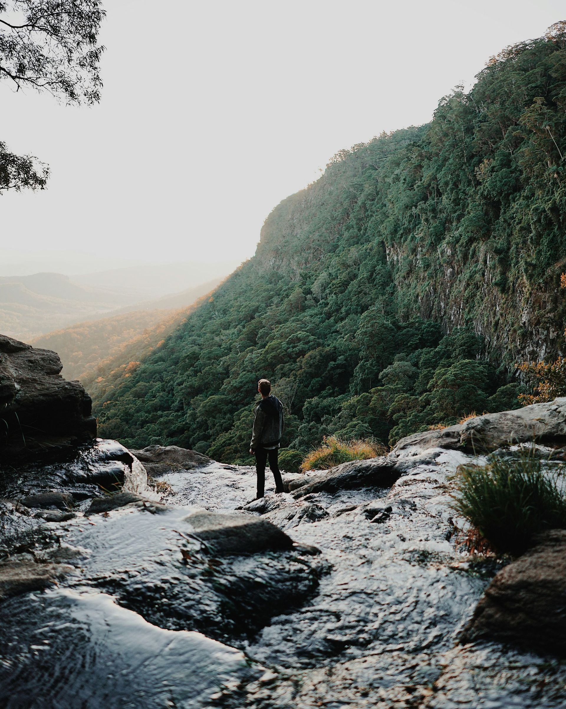 A man is standing on a rock overlooking a river.