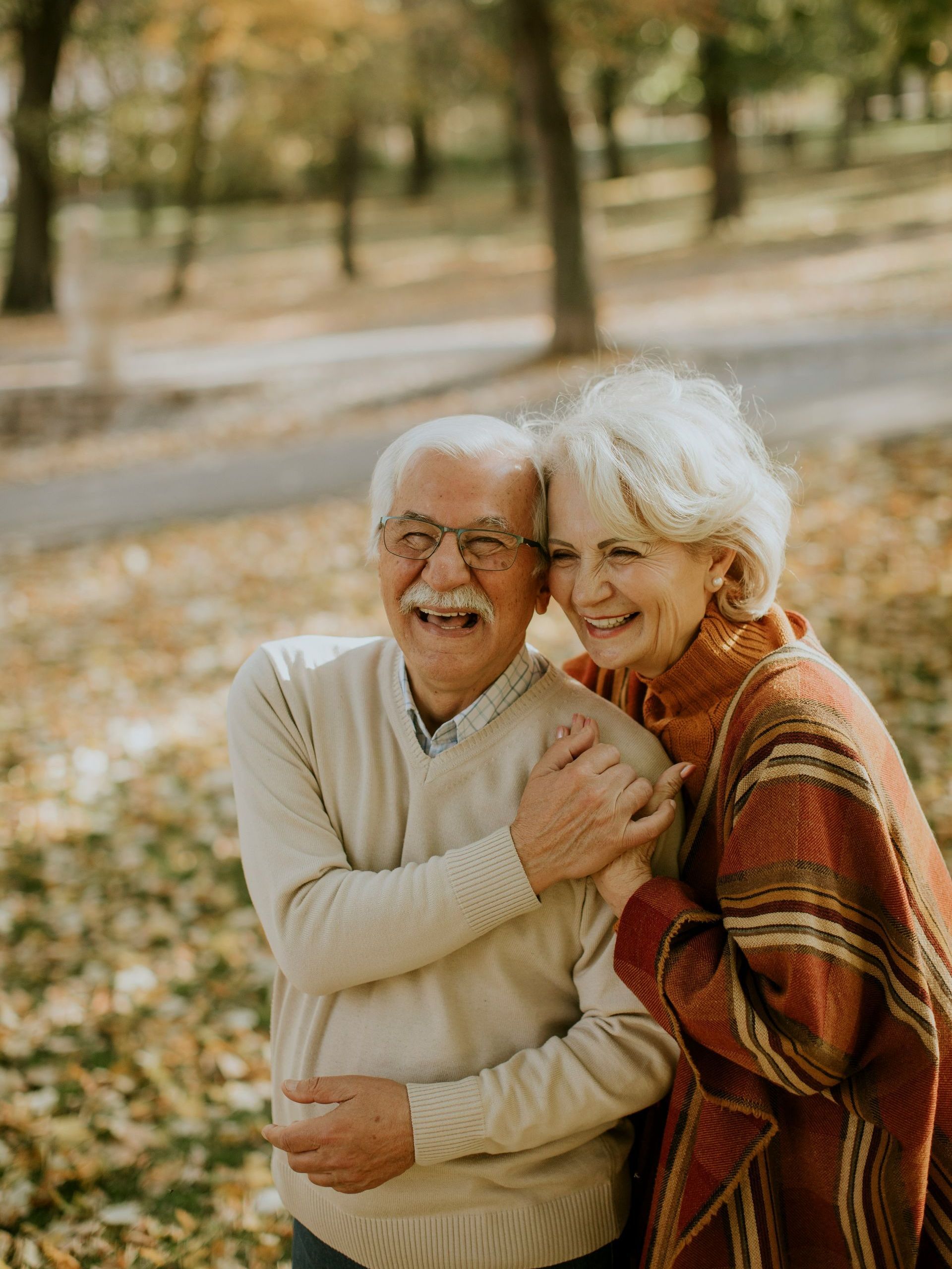 An elderly couple is hugging each other in a park.
