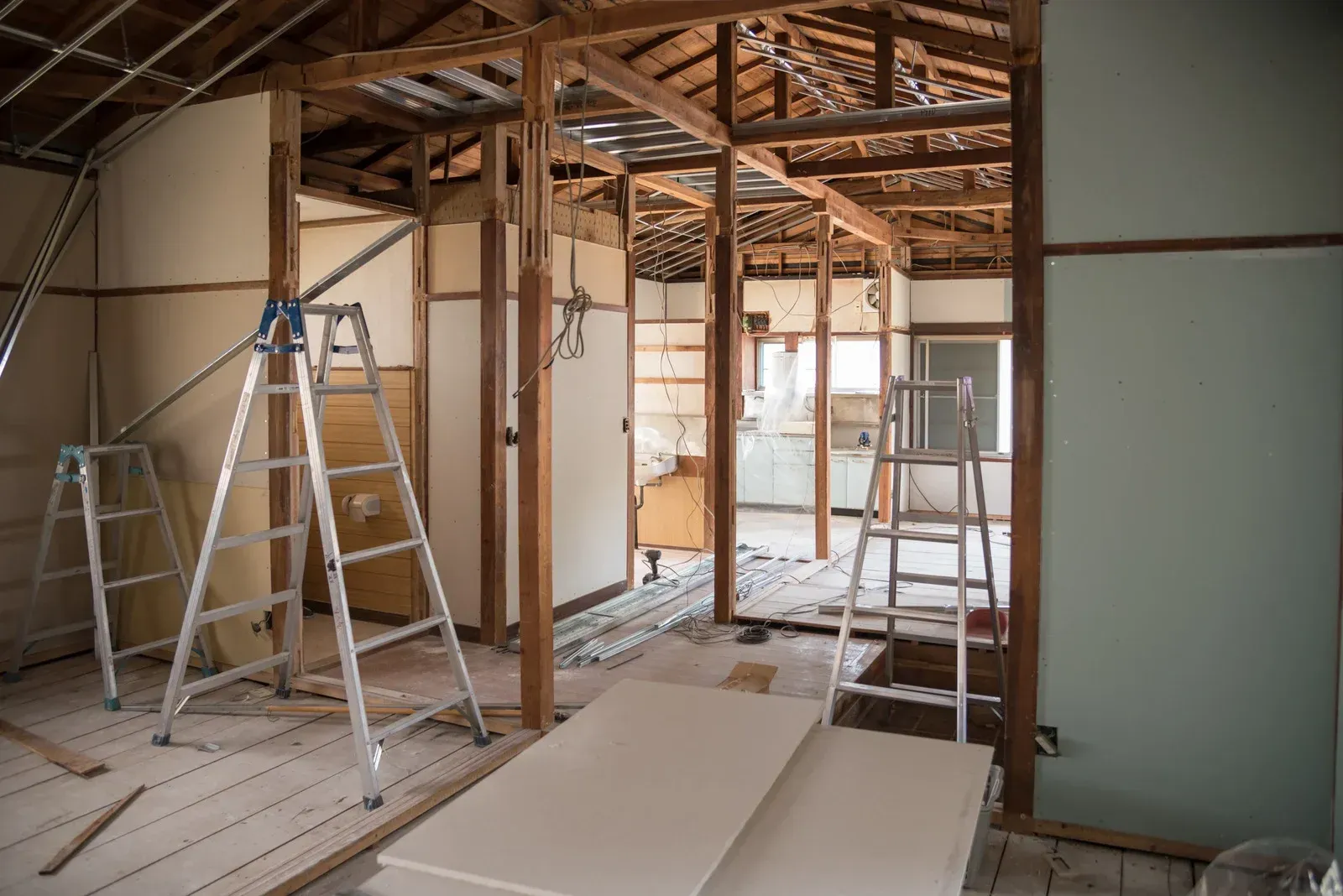 Interior renovation: Exposed wooden beams and studs, ladders, construction materials, and a room's framework.