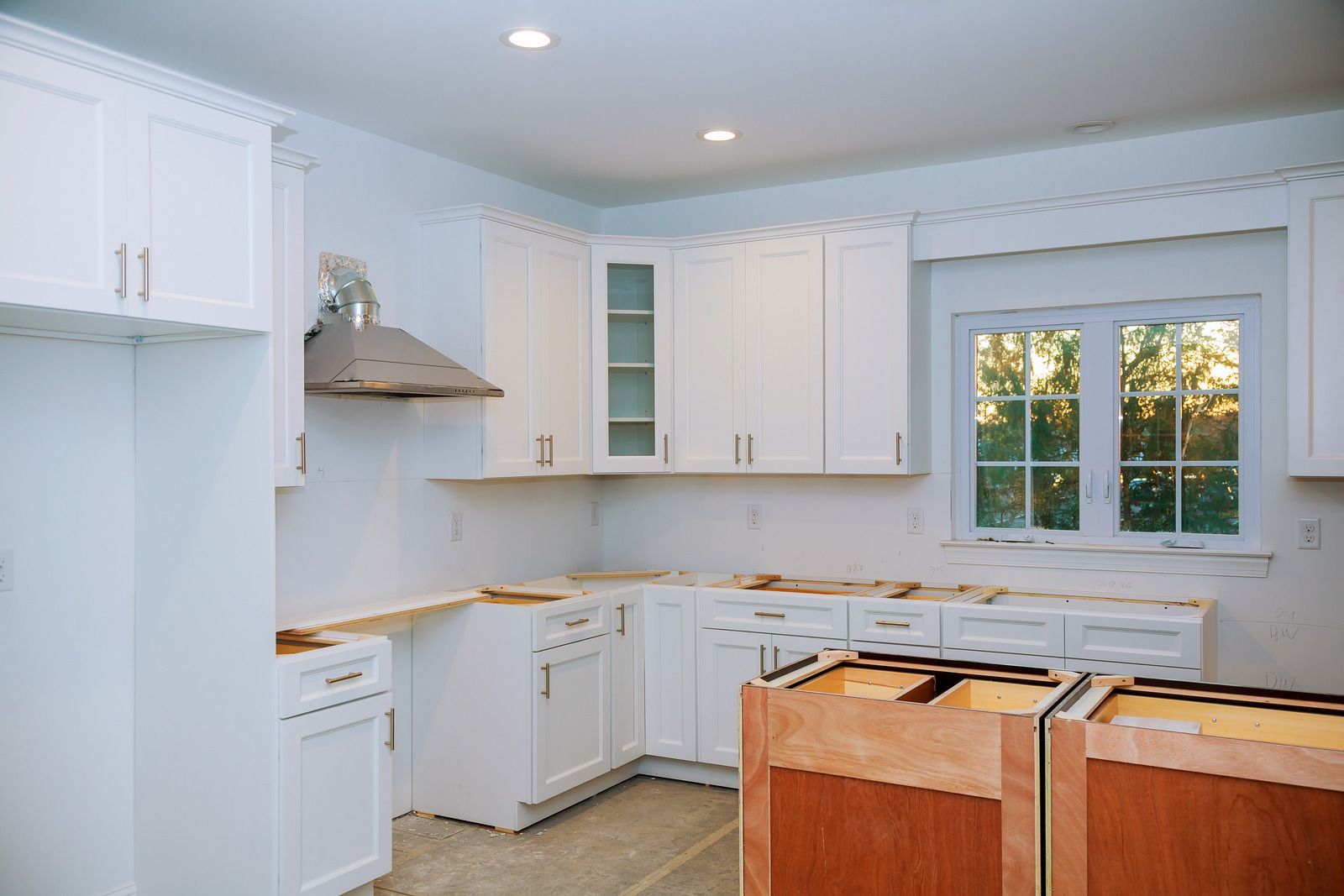 Kitchen under renovation, white cabinets, range hood, window with daylight, unfinished countertops.