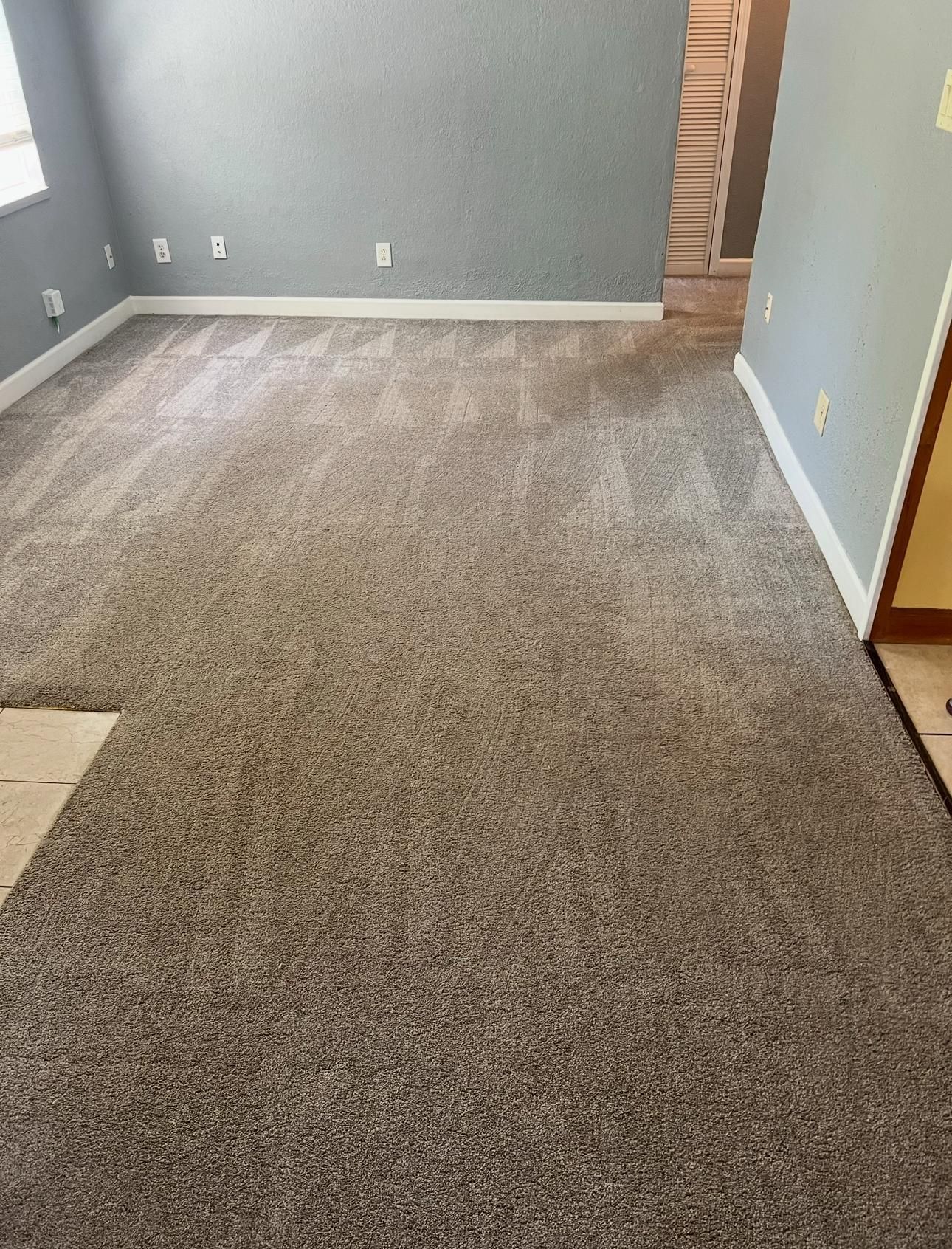 Empty carpeted living room with gray walls and a fireplace opening on the right.