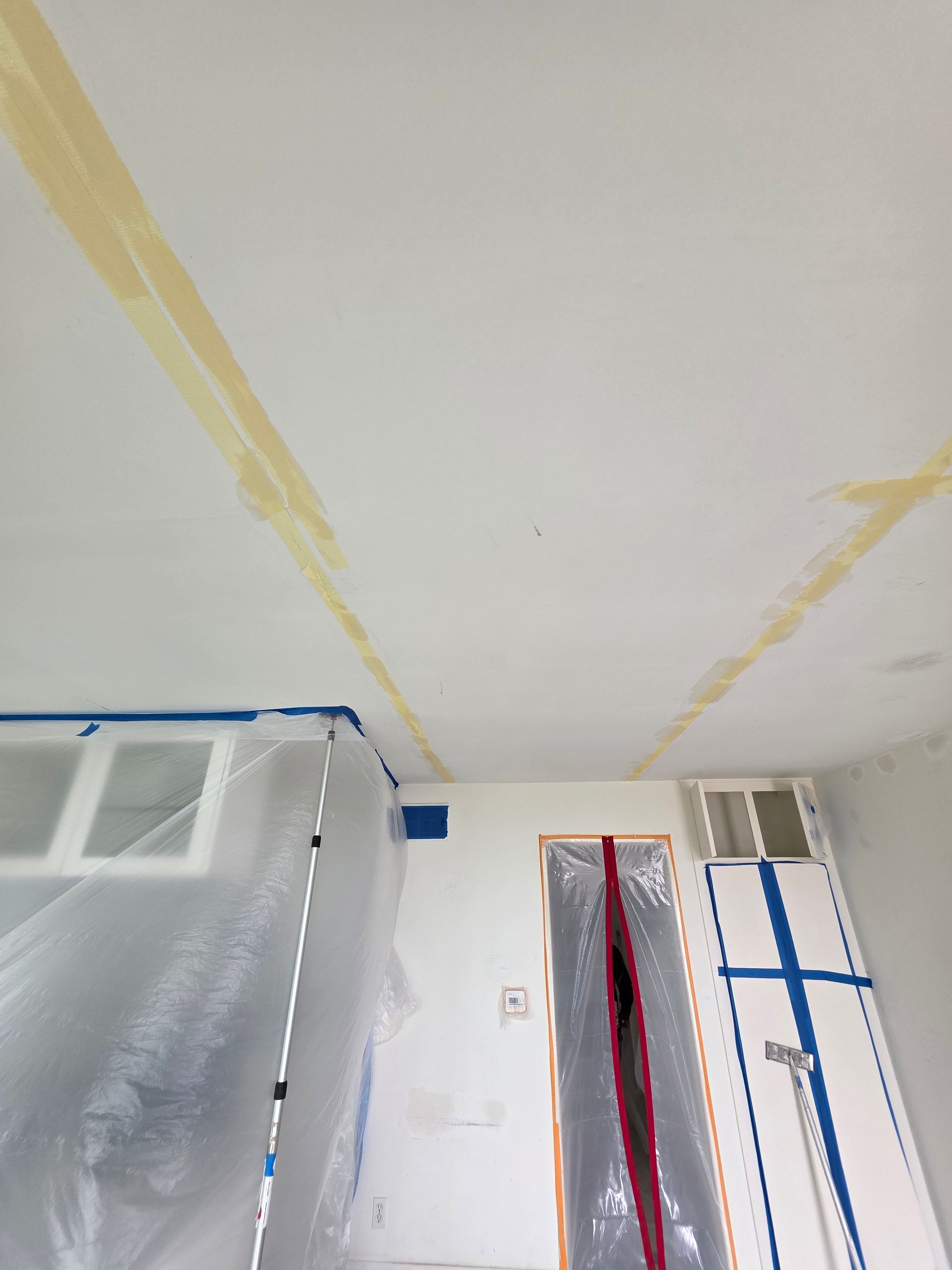 Room interior with masked-off white ceiling, yellow paint lines, and a doorway under renovation.
