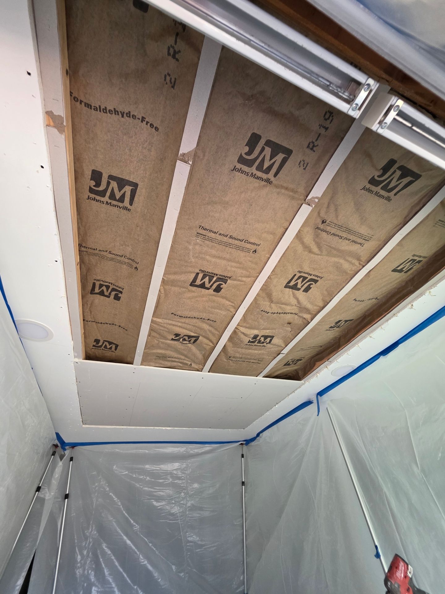 Unfinished ceiling with exposed insulation and plastic sheeting walls in a room under renovation