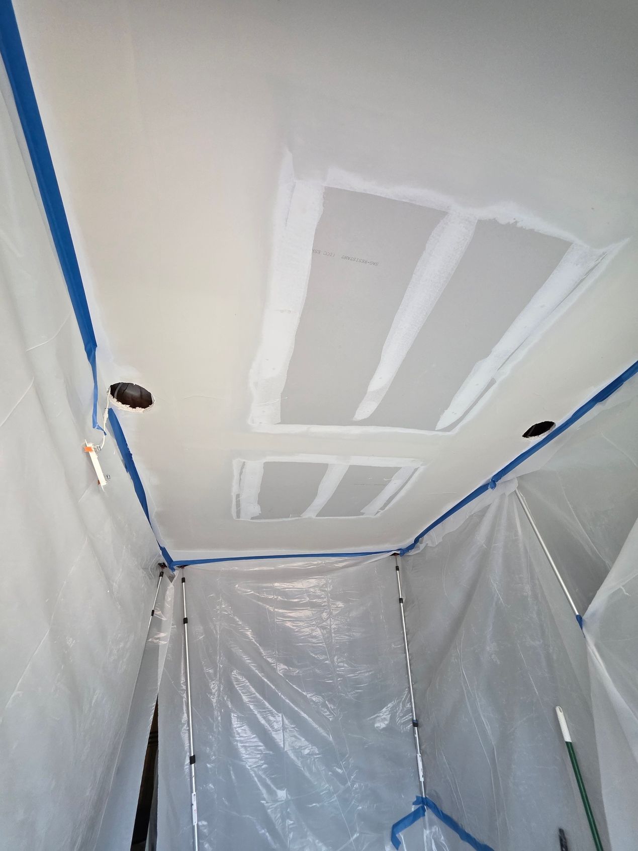 Ceiling under repair with white drywall patches and plastic sheeting covering the room.
