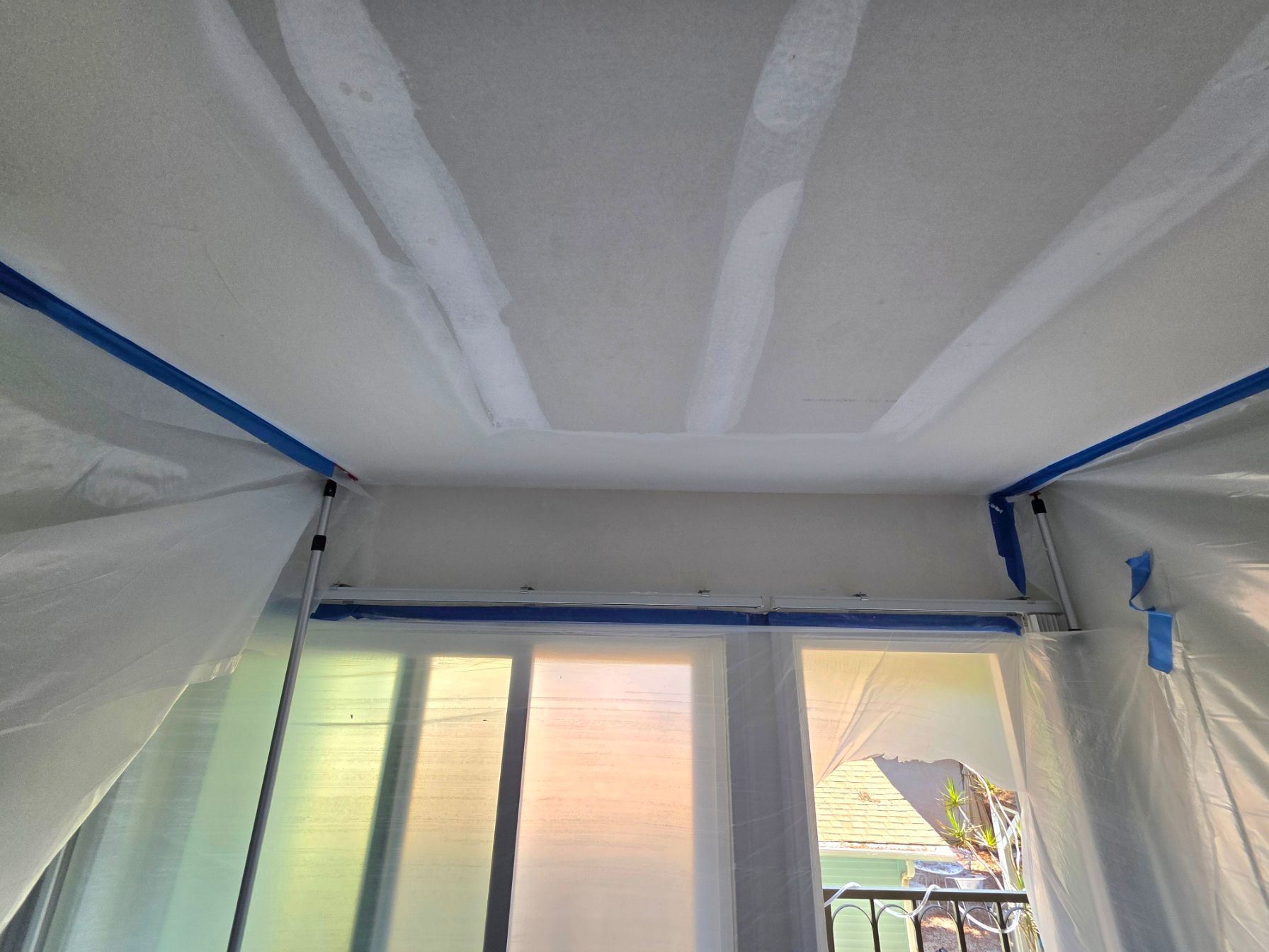 Plastic sheeting covers a room ceiling and walls during renovation, with a window below.