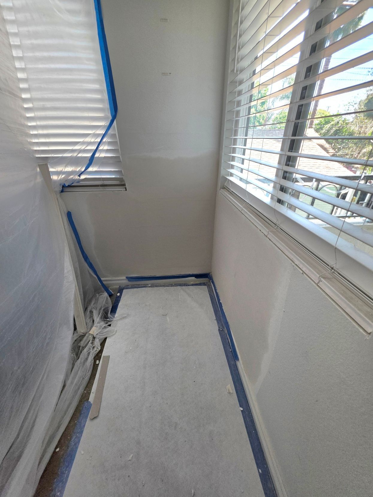 Narrow room with white walls and windows, floors covered for painting or renovation.