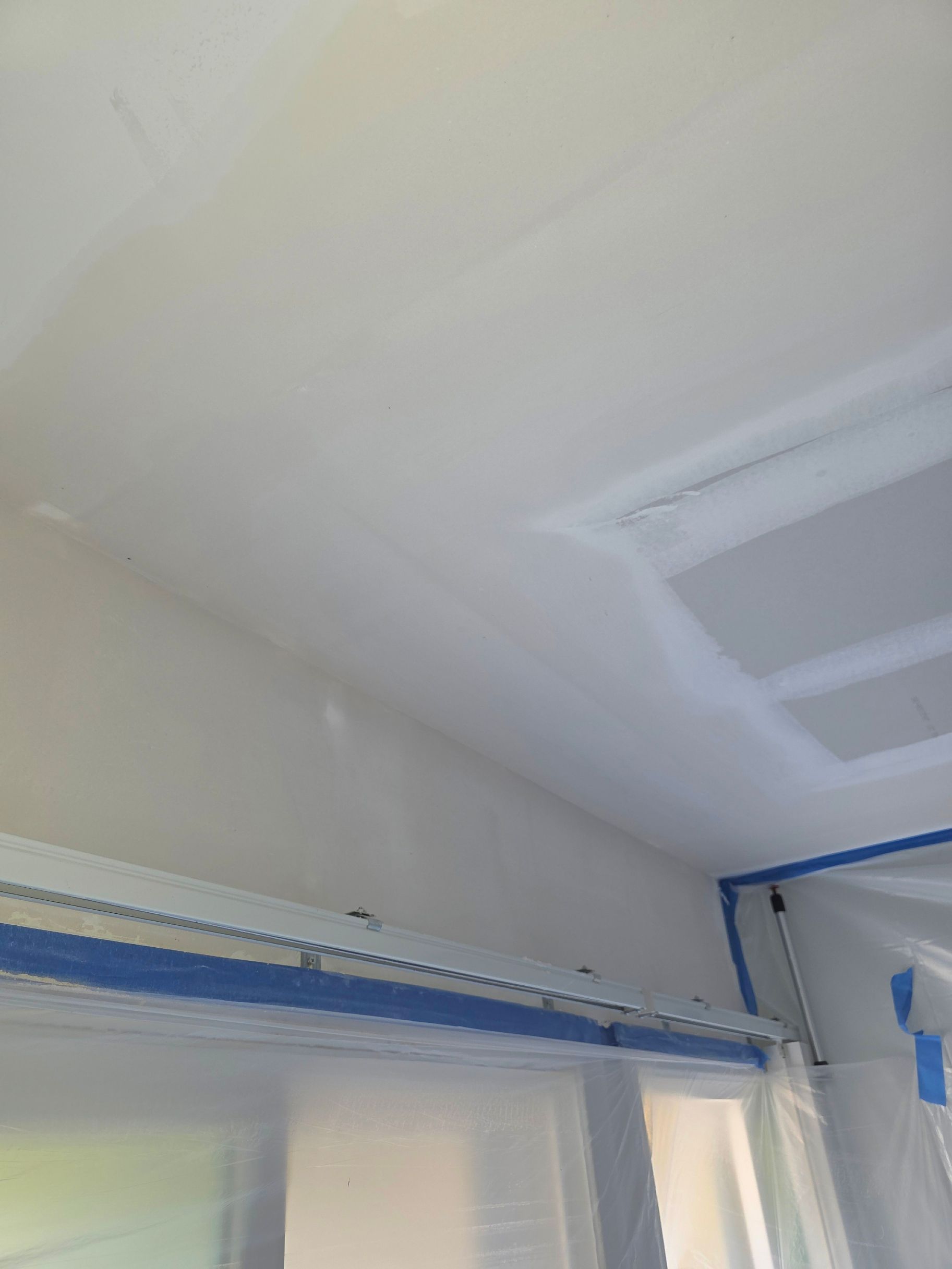 White room ceiling and upper wall with blue painter’s tape around the window trim and corner