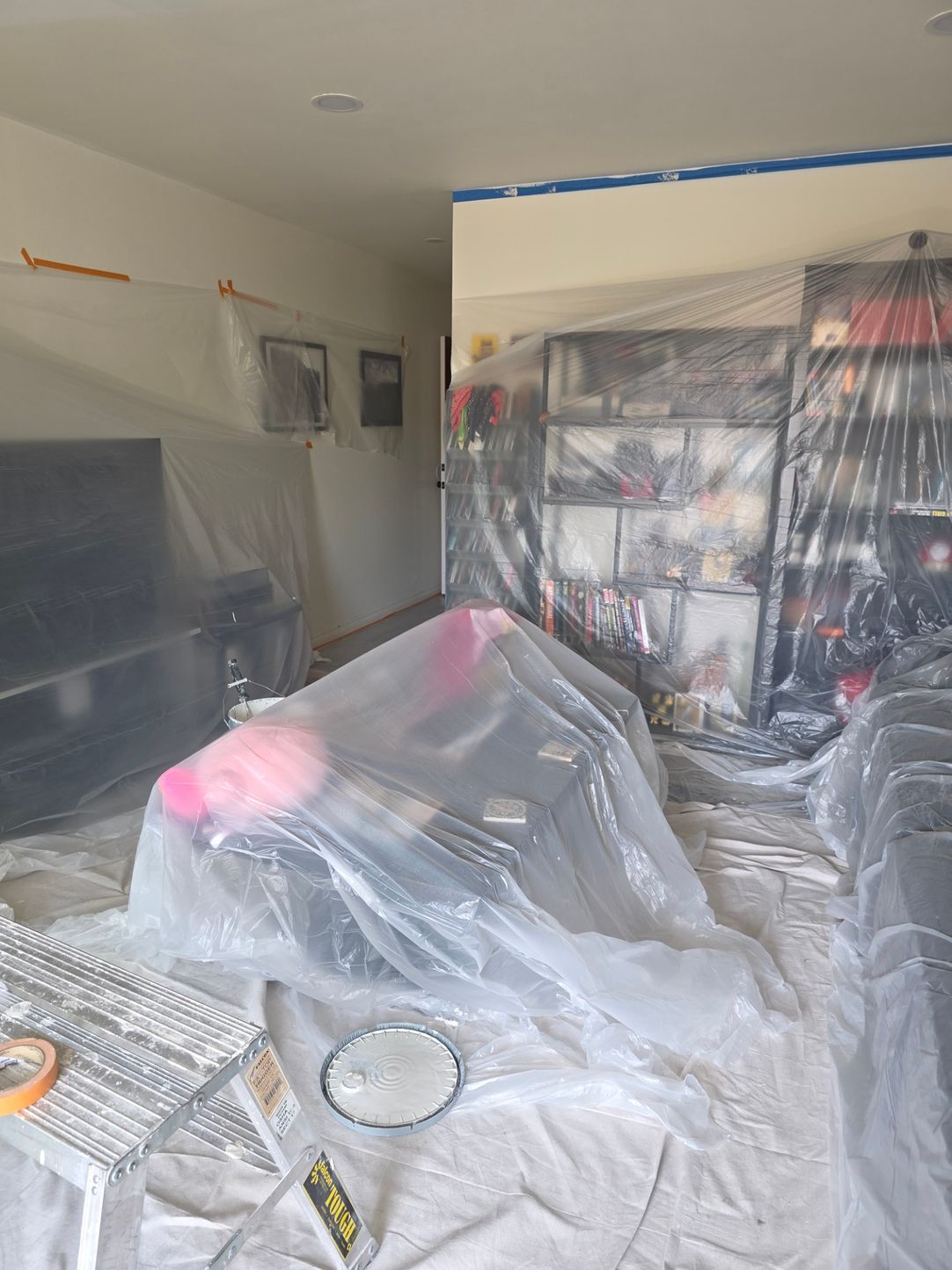 Room under renovation, with furniture covered in plastic sheeting and dust protection.
