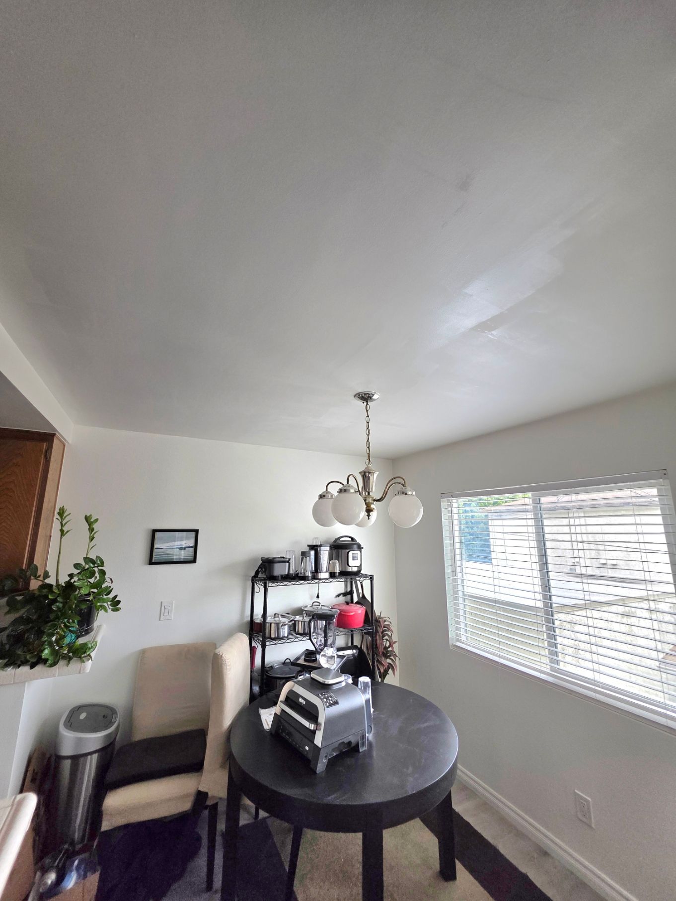 Small dining area with round black table, chairs, shelving, and a window with blinds.