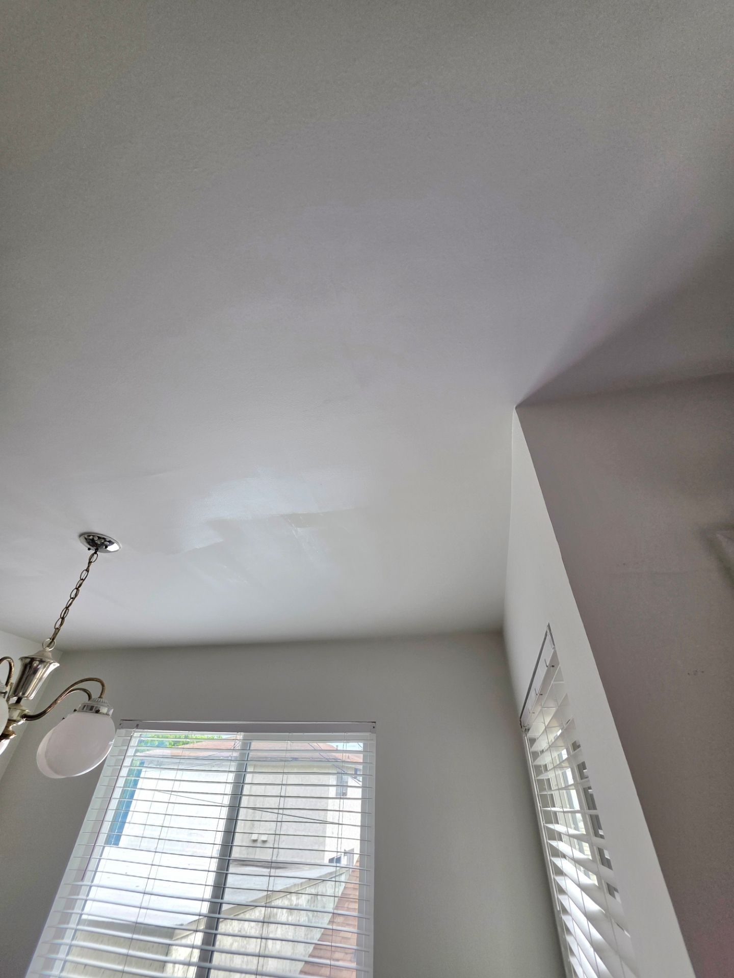 Ceiling corner above a window with white blinds and part of a chandelier indoors