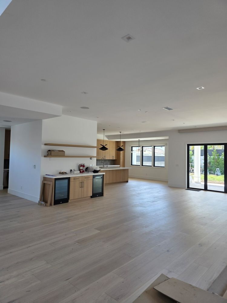Empty modern open-plan living room with light wood floors, white walls, and large glass doors.