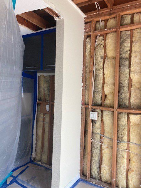 Partially finished room with exposed insulation, studs, drywall, and plastic sheeting during renovation