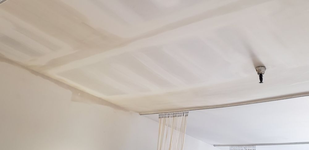 Ceiling corner with drywall patches and a small exposed light fixture