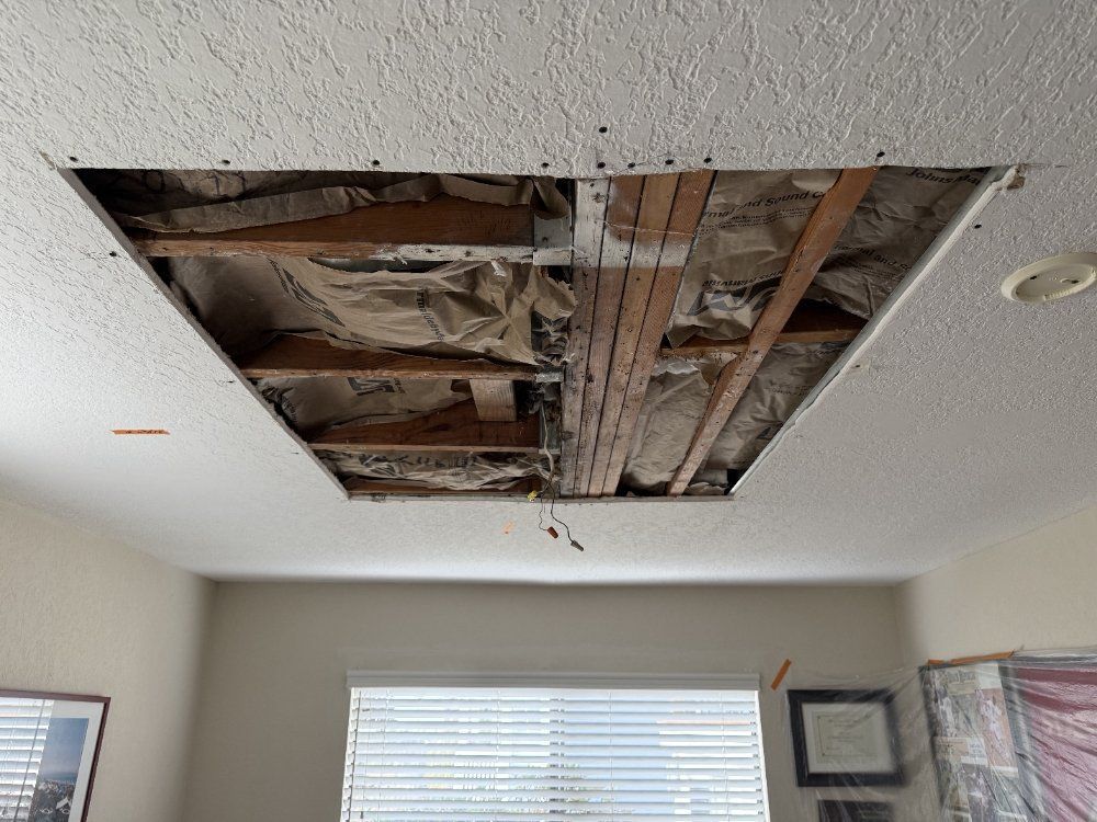 Damaged ceiling with a large exposed hole, showing insulation and wooden framing in a room
