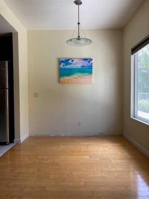 Empty dining room with hardwood floor, pendant light, and small beach painting on cream wall