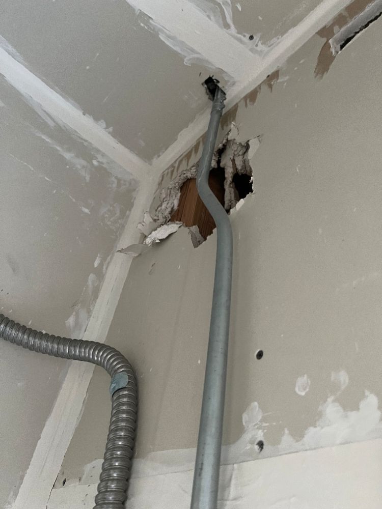 Ceiling corner with exposed gray conduit and damaged drywall around an opening