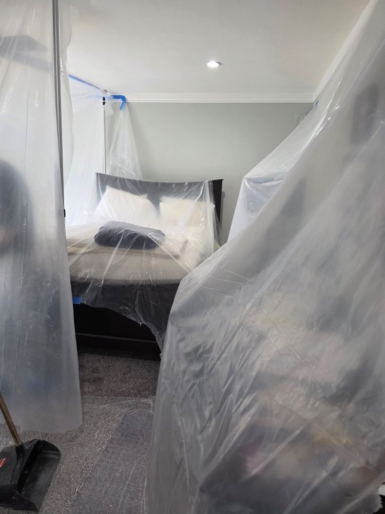 Bedroom under renovation, furniture covered in clear plastic sheets.