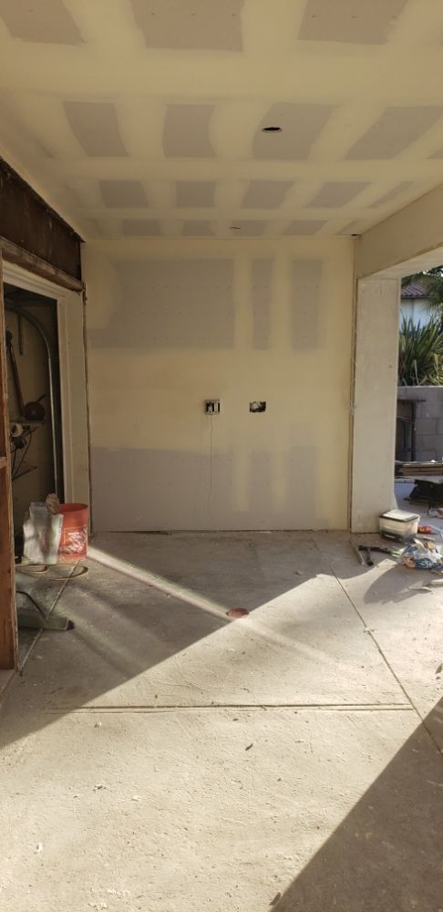 Covered driveway with unfinished drywall and concrete floor, sunlight streaming in from the right.