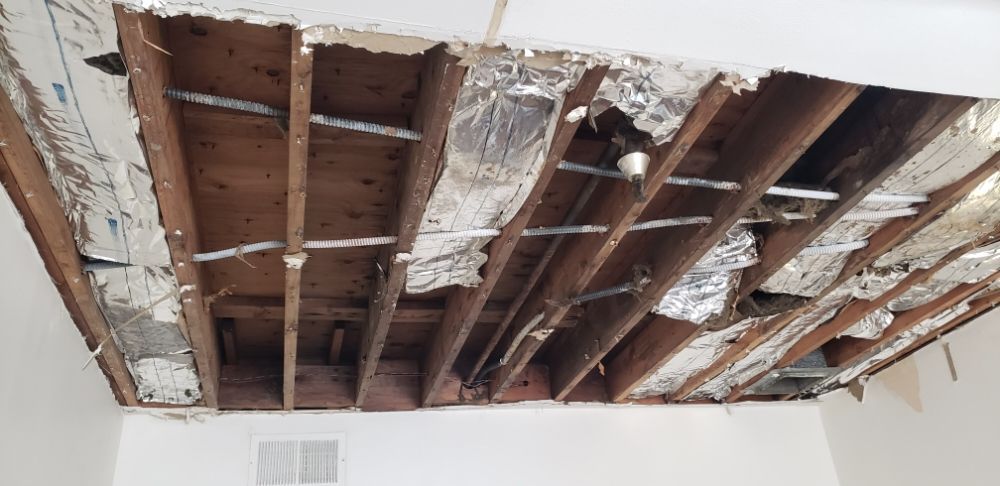 Exposed ceiling joists and damaged drywall with insulation hanging down in a room