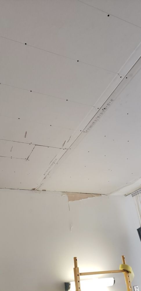 Damaged white ceiling with cracks and a missing section above a yellow ladder