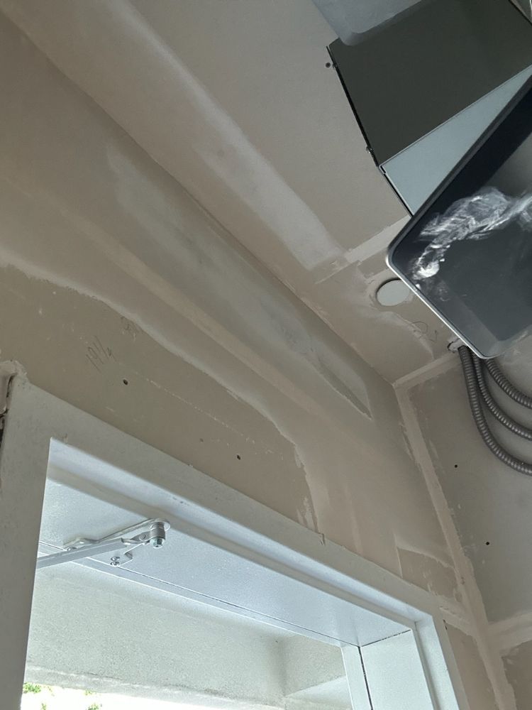Ceiling and doorway interior with visible drywall seams and a mounted black device in the corner